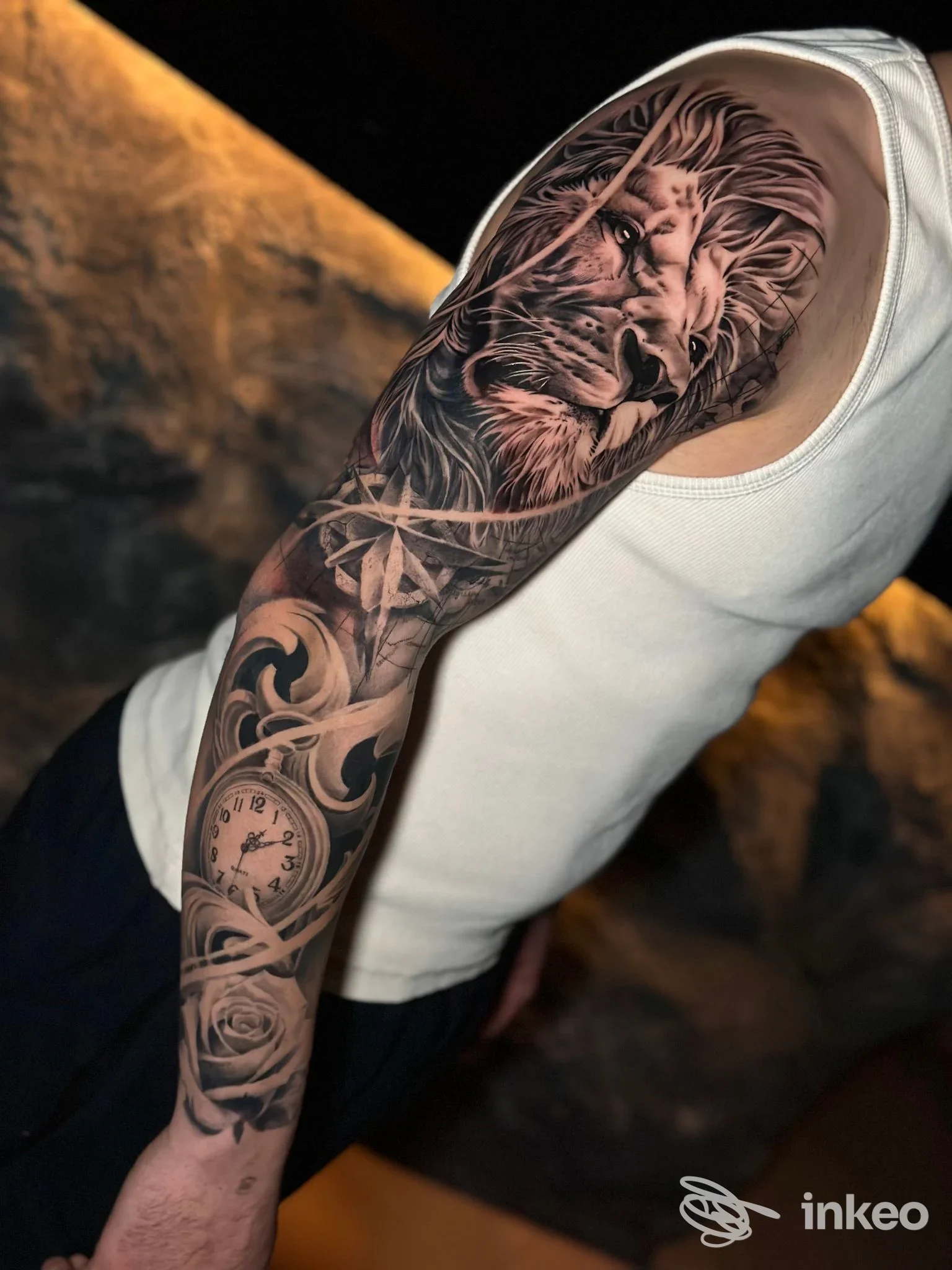 Manica tatuata realistico in bianco e nero con leone, rose e orologio sul braccio destro, immagine per District Tattoo Studio, Castelvetro Piacentino.