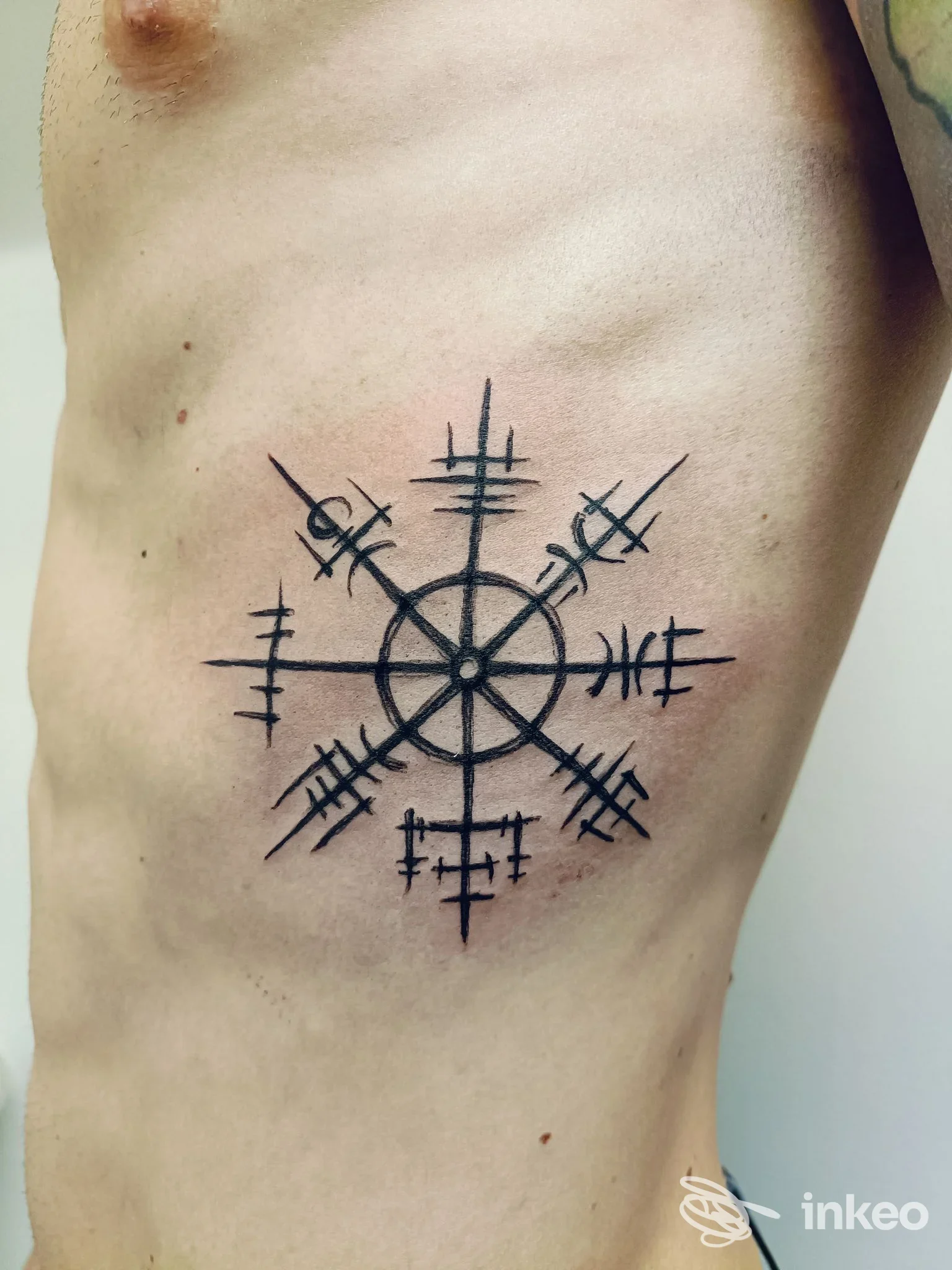 Tattoo a forma di bussola stilizzata con linee nere su pelle chiara, situata sul torace sinistro. Nessun volto visibile.Nel contesto Notaricon Tatuaggi, città non specificata.