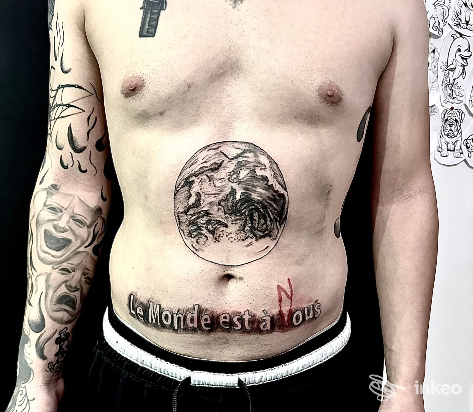 Addome maschile con tatuaggio centrale a forma di globo e scritta 'Le Monde est à Nous'; foto di Icarus Tattoo & Portrait, Cadelbosco di Sopra.