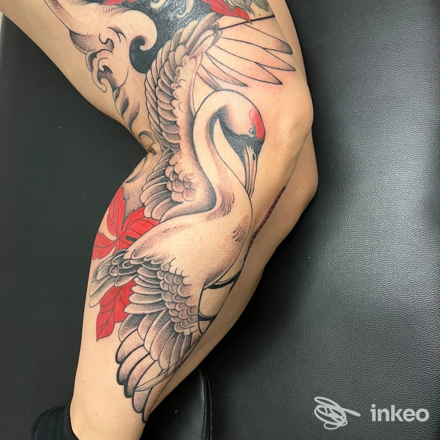 Tattoo sulla gamba sinistra: uccello stilizzato con piume e dettagli neri, grigi con riflessi rossi, realizzato sulla pelle reale.