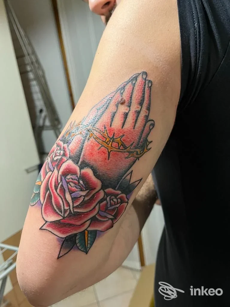 Primo piano di un tatuaggio sul braccio con mani giunte e rose, fotografato da Freak Show Tattoo a Cesena.