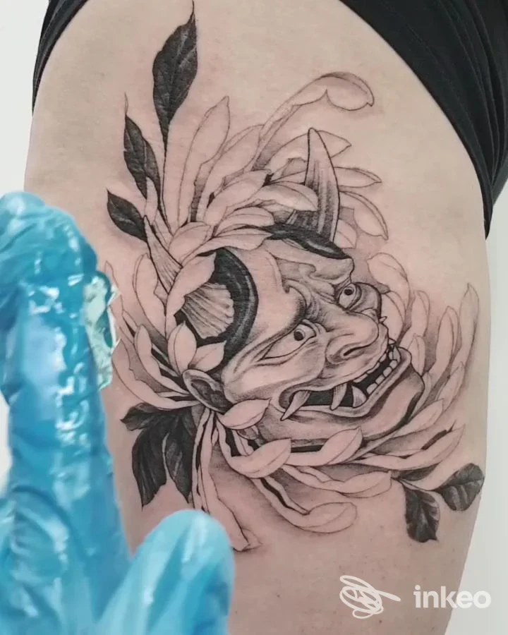 Tatuaggio in bianco e nero raffigurante una maschera e foglie sulla coscia. Novytattoo Handmade Tattoo Studio, Carpi.