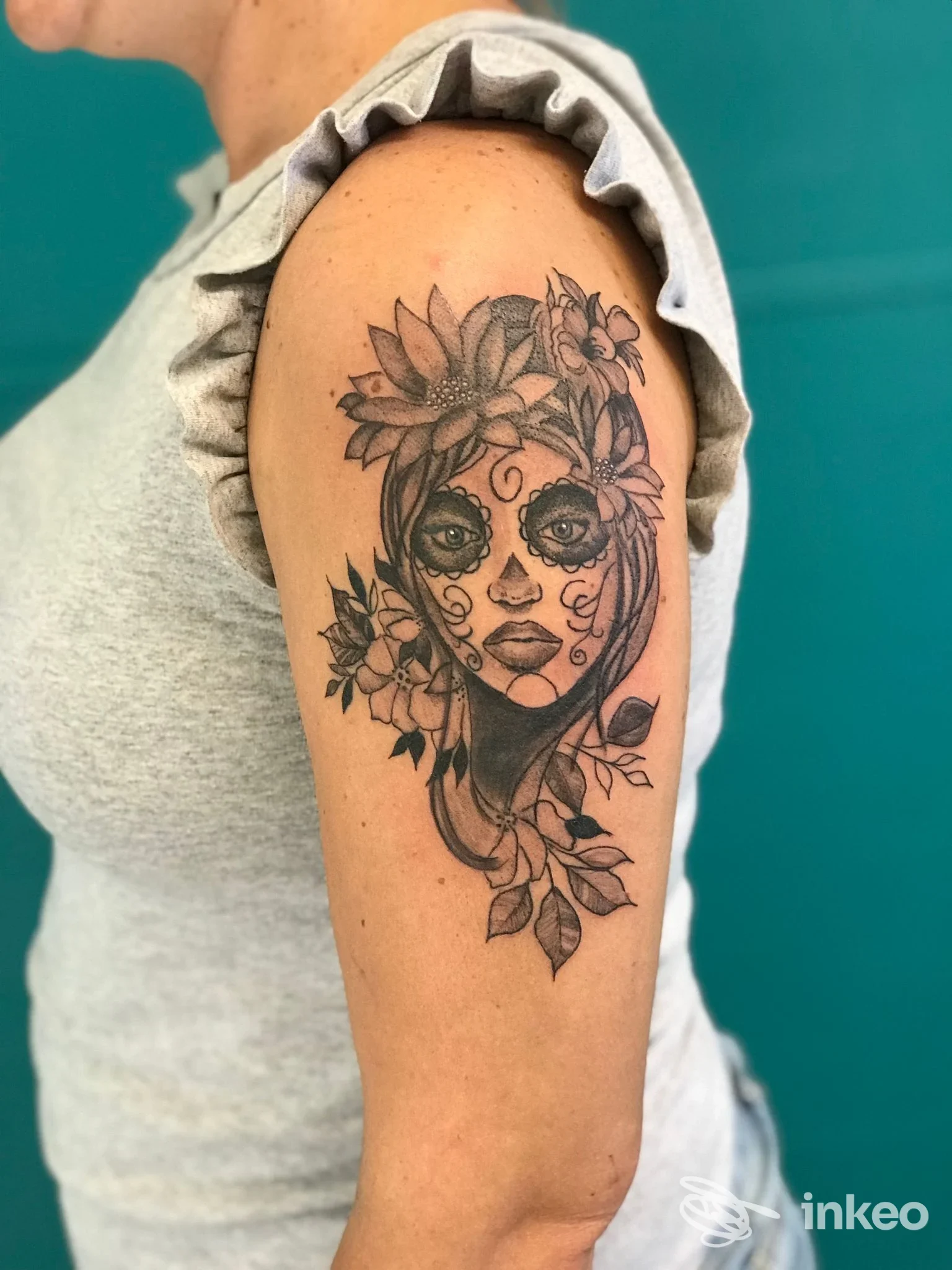 Tatuaggio in bianco e nero a forma di volto femminile con fiori sul braccio superiore, fotografia fornita da Natattoo Studio, Forlì.
