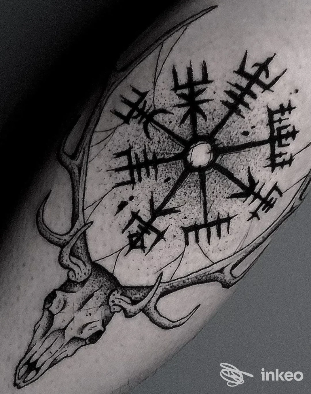 Tatuaggio in bianco e nero: teschio di cervo con corna e simbolo runico circolare su avambraccio. Eleven ink, Piacenza.