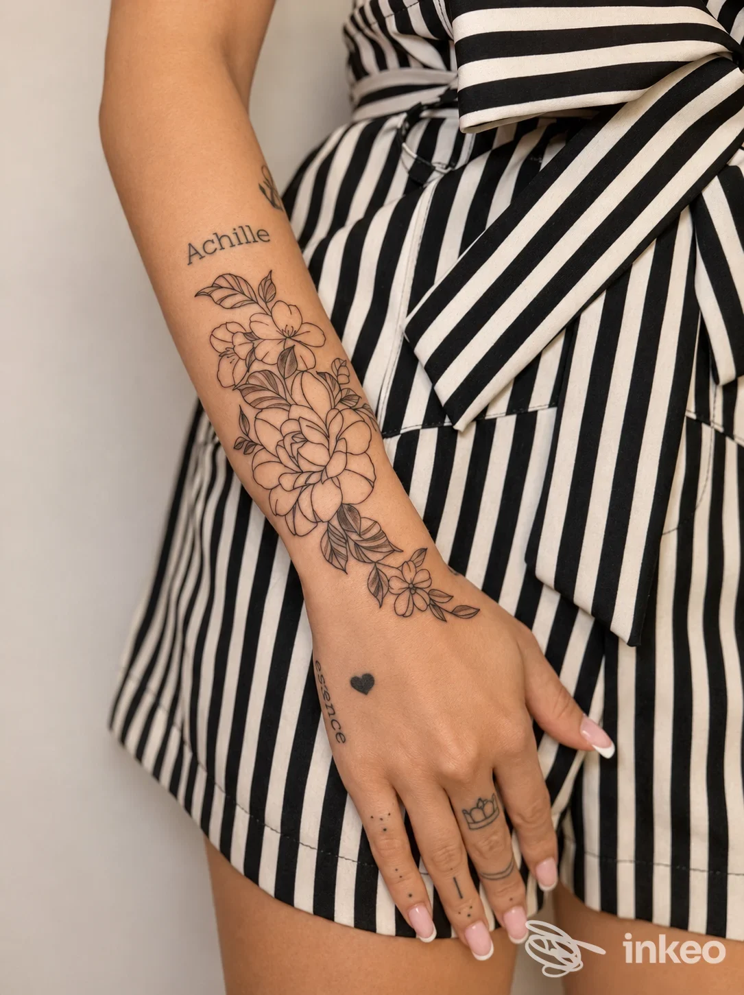 Avambraccio tatuato con motivo floreale nero e scritta 'Achille', mano con piccolo cuore. Foto per Green Frog Tattoo Parlour, Bellaria-Igea Marina.