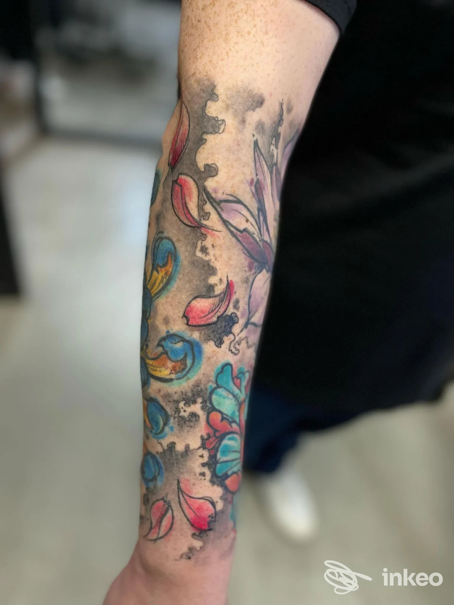 Avambraccio tatuato con motivi floreali e petali colorati, foto fornita da C.Ink Tattoo a Cesenatico.