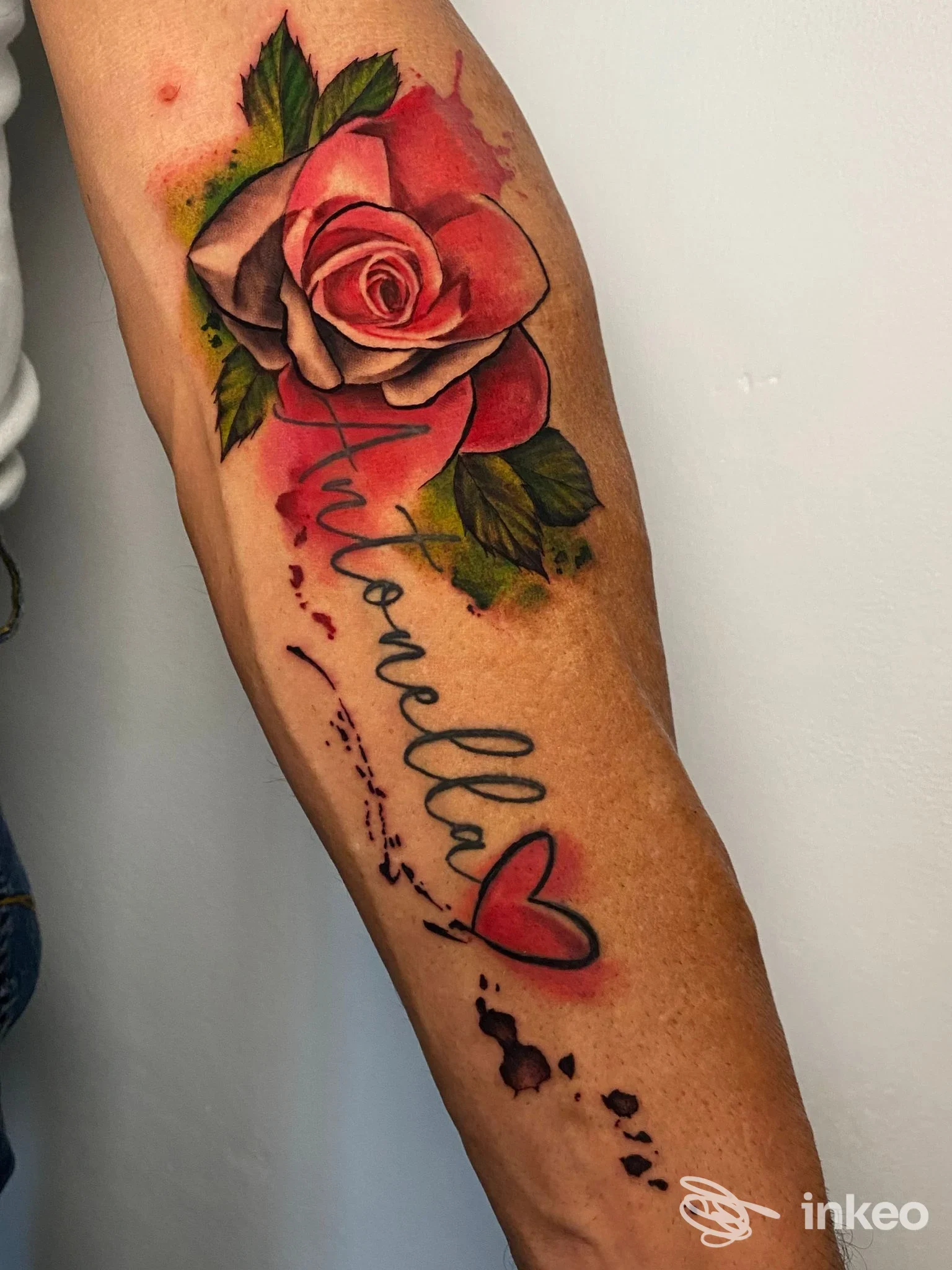 Tatuaggio realistico di rosa rossa sul braccio con scritta corsiva e piccolo cuore, realizzato da Alex Tattoo, città non specificata.