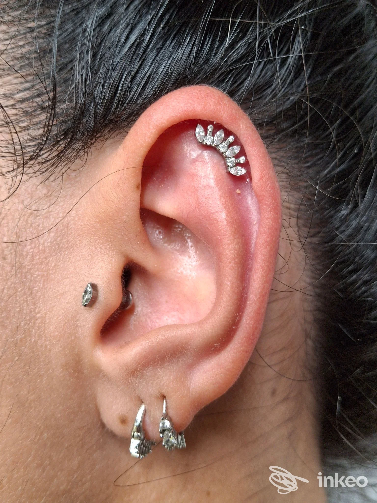 Primo piano di un orecchio con più piercing e gemme, foto fornita da art studio tattoo a Pavullo nel Frignano.
