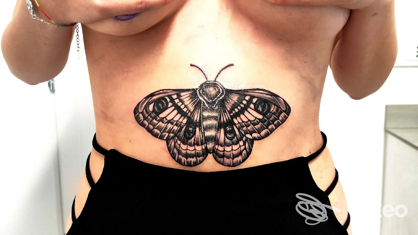 Grande tatuaggio a forma di falena in nero posizionato sul basso sterno/addome superiore, foto per Porka Loca Tattoo Studio, Ravenna.