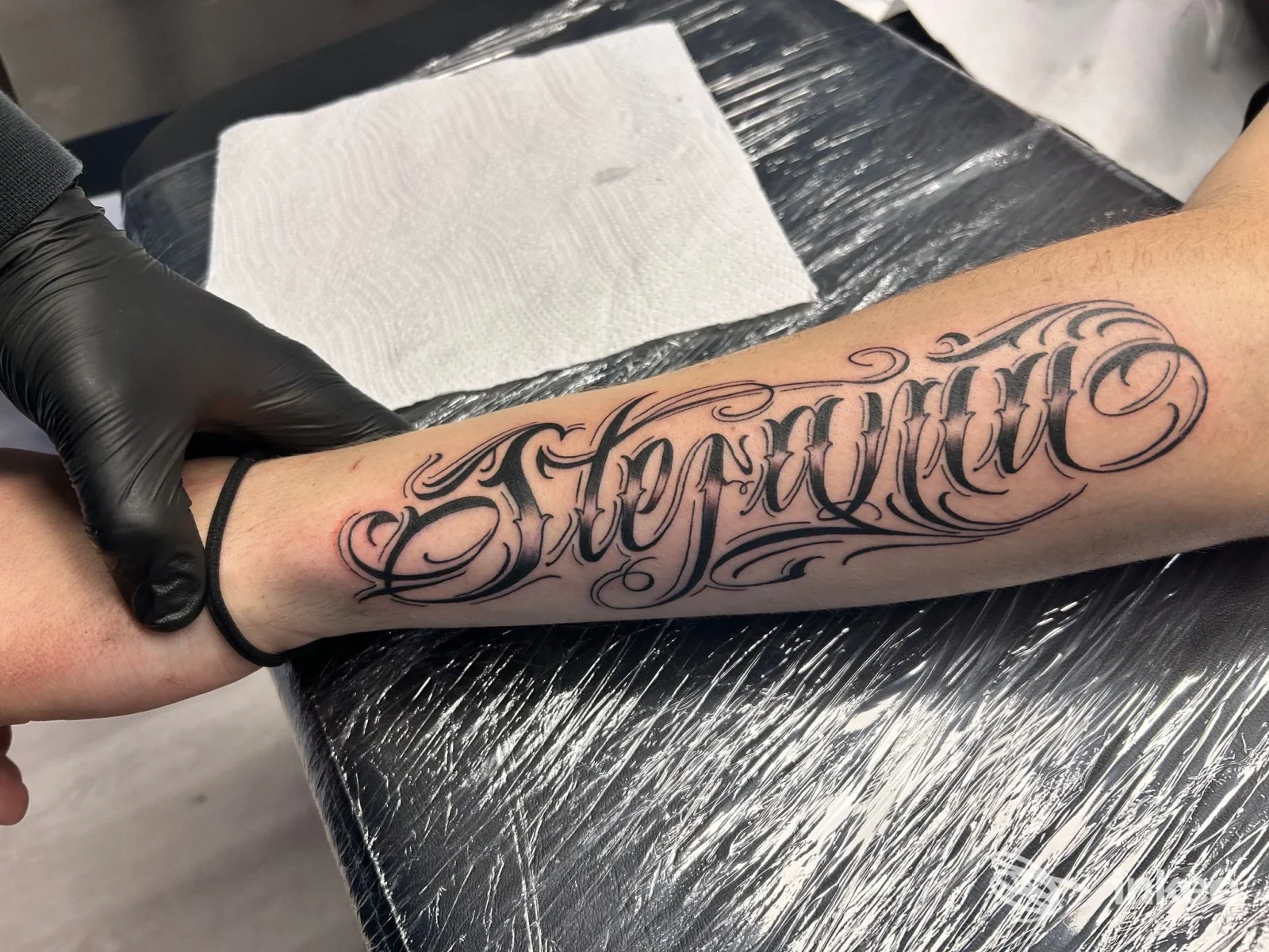 Tatuaggio lettering ornamentale in nero sull'avambraccio, fotografato nello studio Daniel Dandi 17 Tattoo a Roveleto.