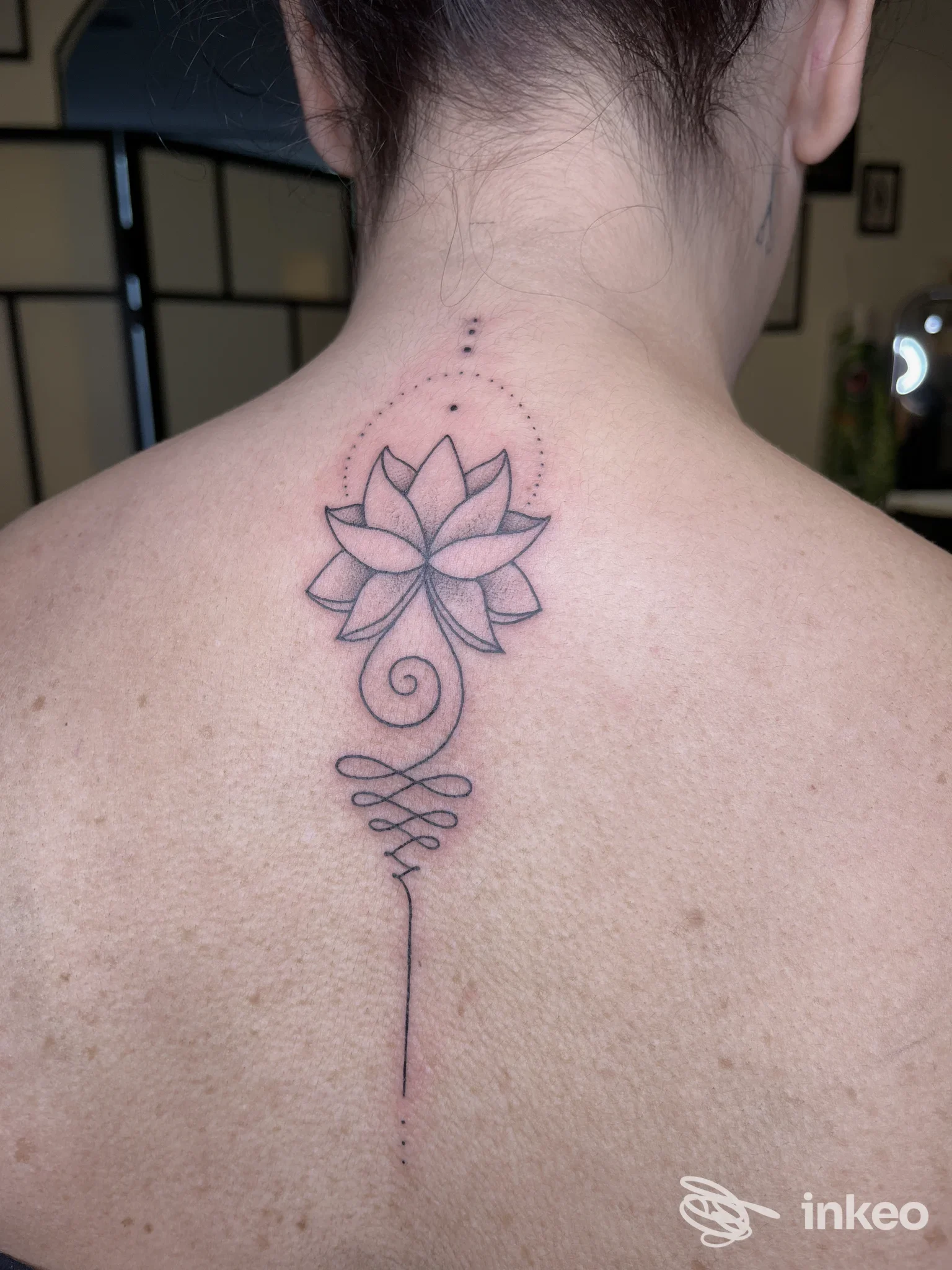 Tatuaggio a inchiostro nero di un fiore di loto con elementi puntinati sulla parte superiore della schiena, Lineanomala, Crevalcore