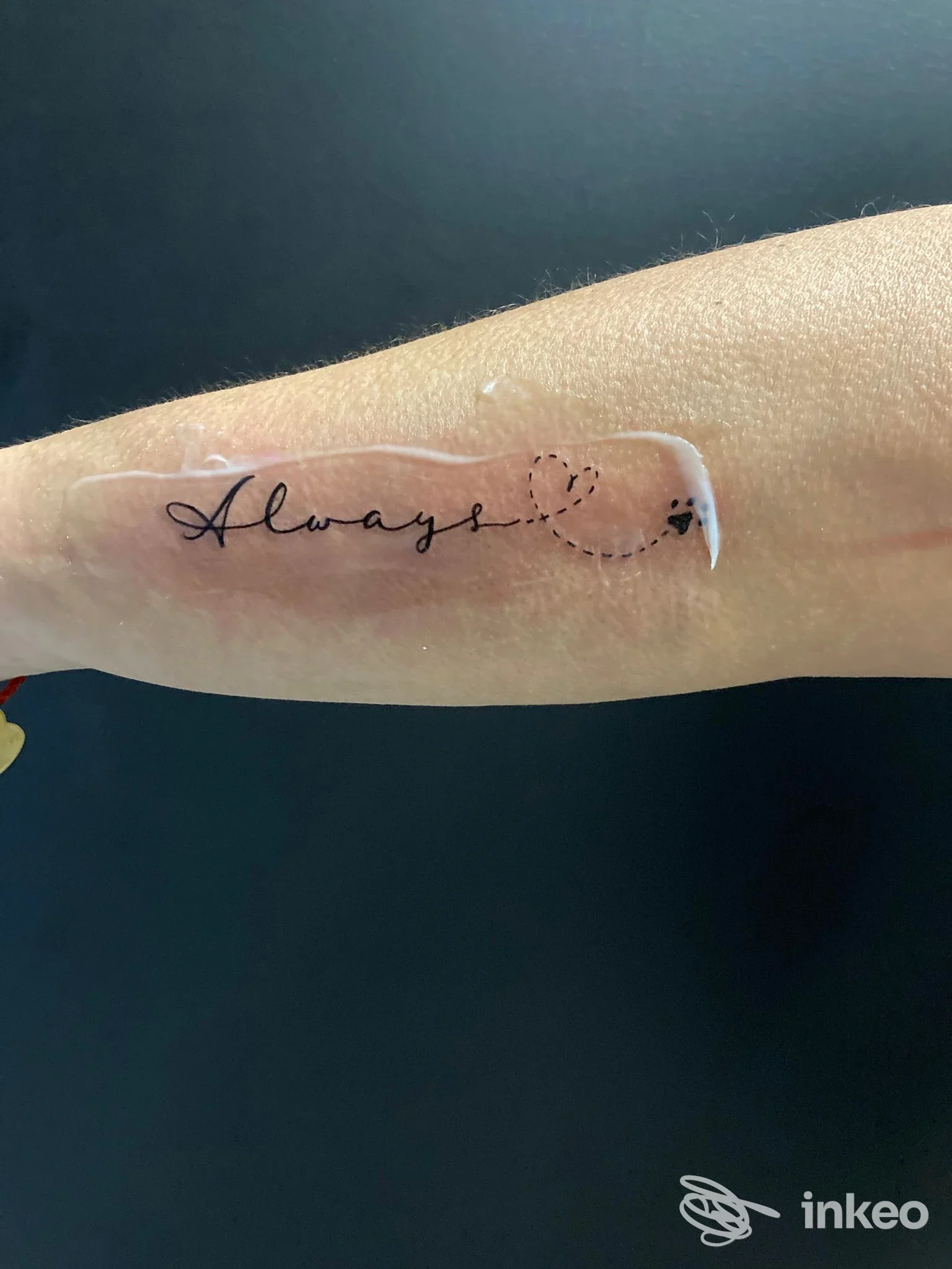 Avambraccio con tatuaggio sottile: la parola Always in corsivo nero lungo una linea, con puntini; realizzato sulla pelle, visibile sulle braccia, firma del tatuaggio AliceFox Tattoo (località non specificata).