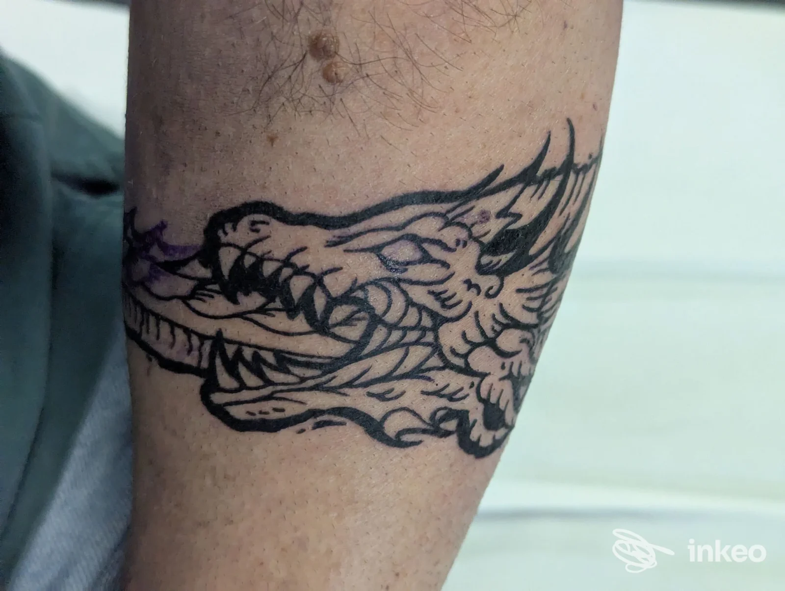 Dettaglio di un tatuaggio nero stilizzato a forma di testa di drago sull'avambraccio, Black Sin Tattoo Studio, Cesena.