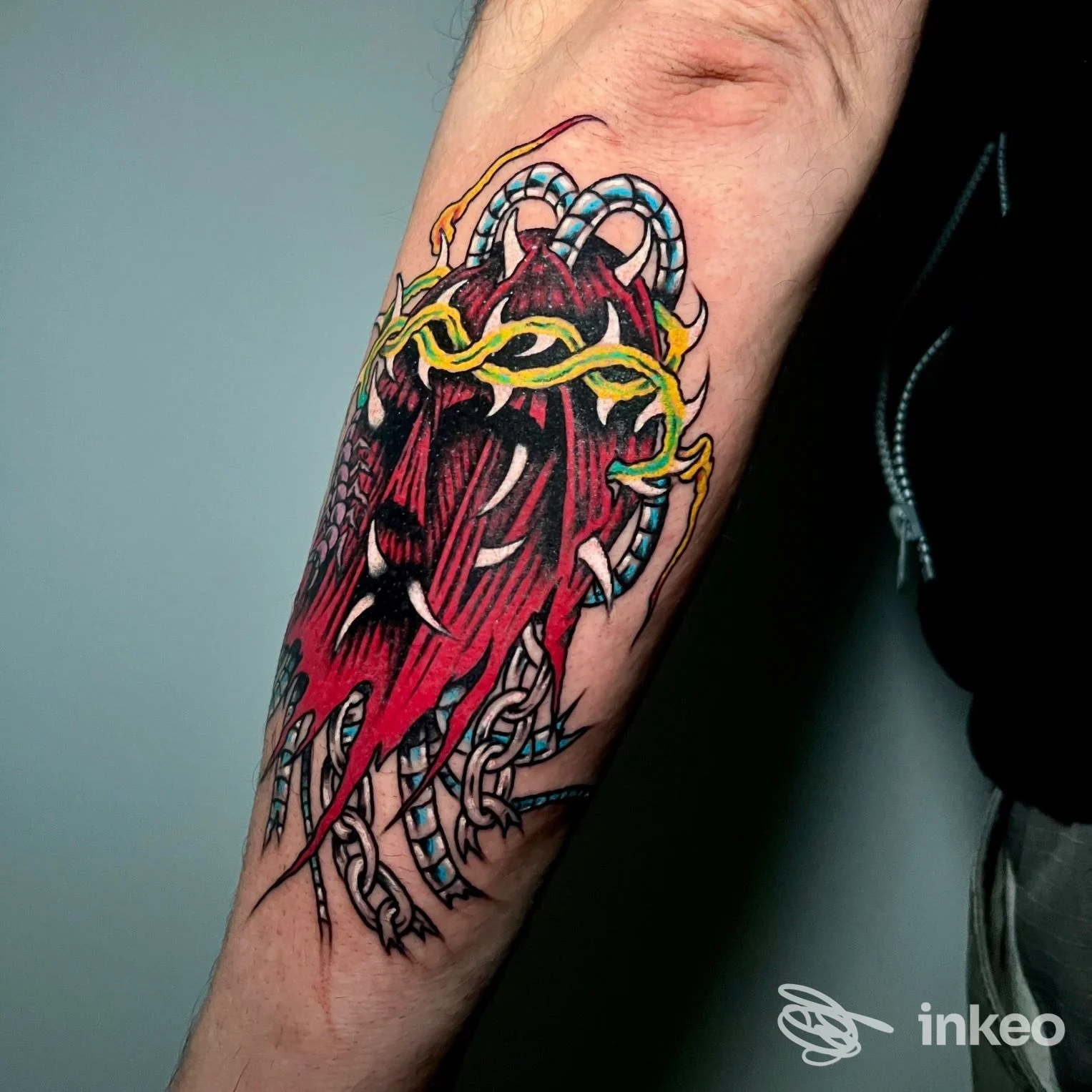 Tatuaggio colorato sul sottoavambraccio con motivo rosso, catene blu e dettagli gialli, scattato presso Homeless Tattoo Piercing & Streetwear a Piacenza.