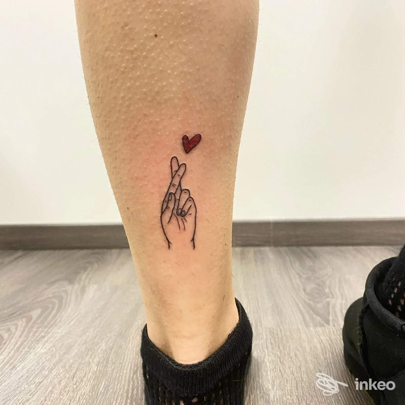 Tatuaggio su polpaccio: mano con dita incrociate in linee nere e piccolo cuore rosso. Cuore Nero Tattoo, Fornace.