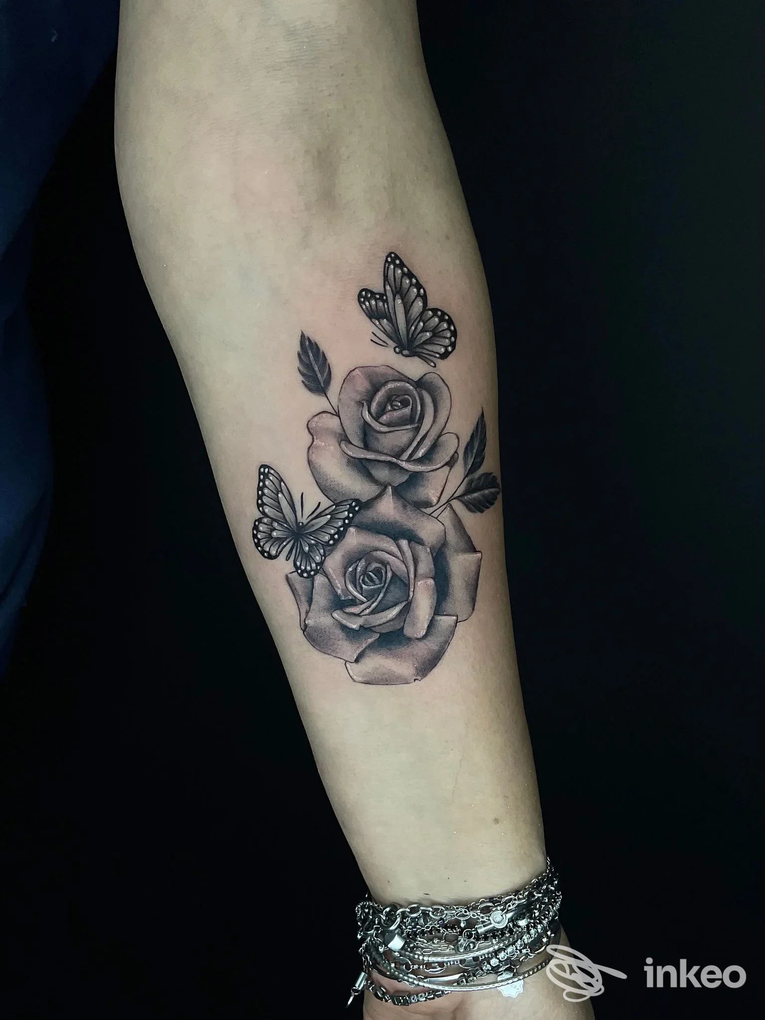 Due rose e due farfalle tatuate in bianco e nero sull'avambraccio, lavoro realizzato presso InkWish, Cattolica.