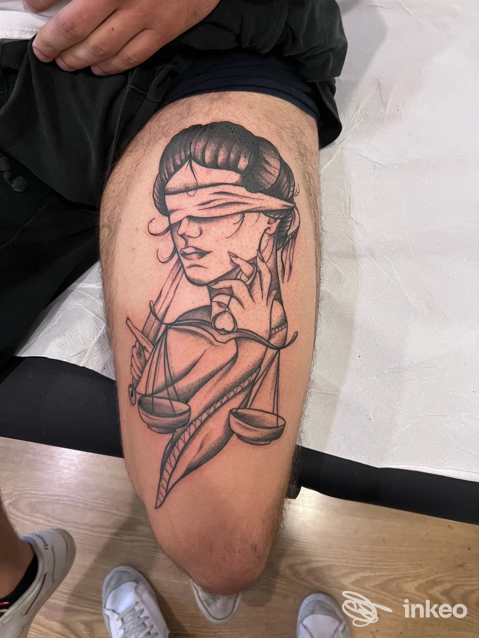 Tatuaggio in bianco e nero su coscia raffigurante figura bendata con bilancia, foto dallo studio Bear tattoo studio a Reggio nell'Emilia.