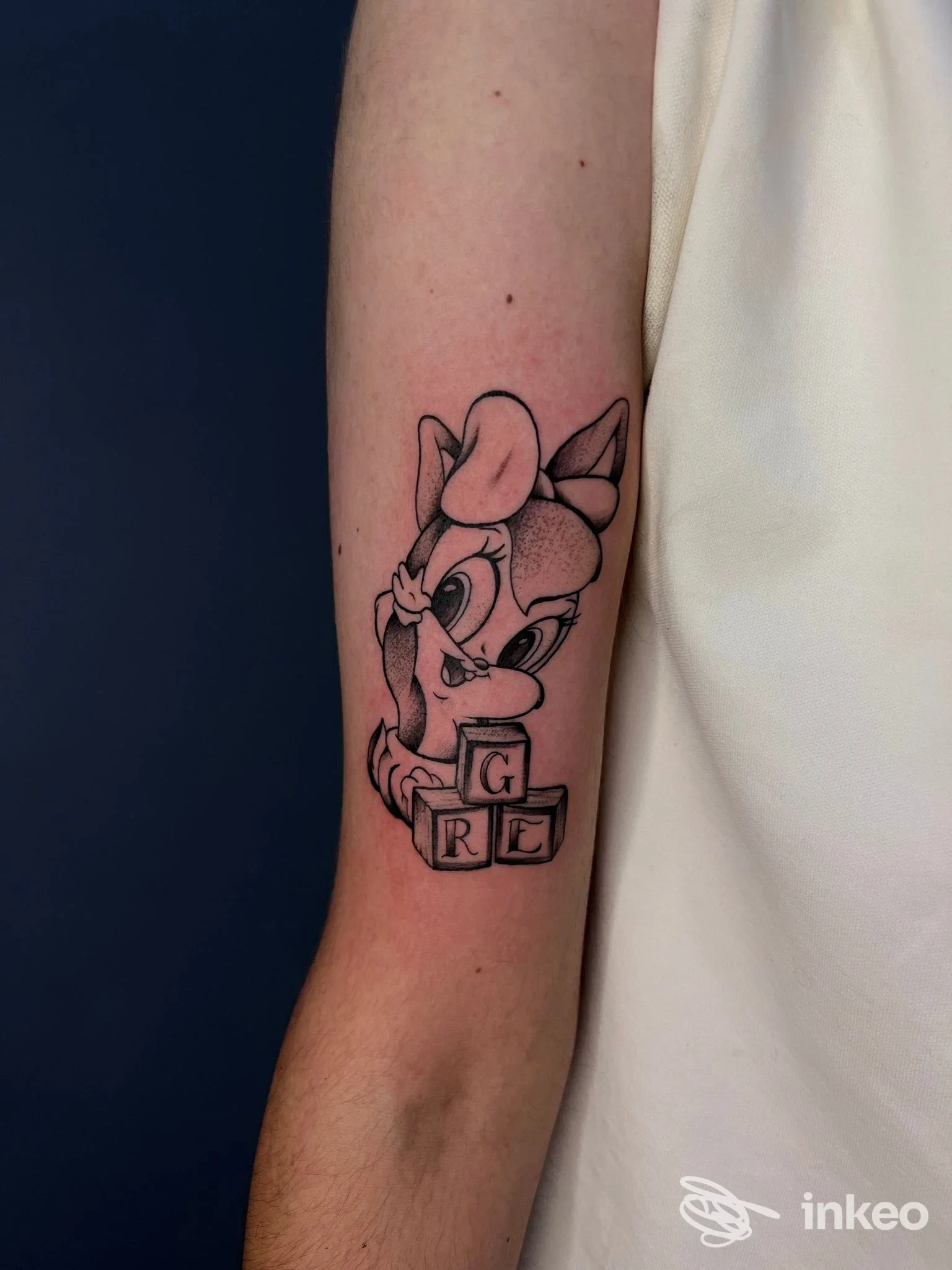 Tatuaggio in nero su avambraccio interno raffigurante un personaggio cartoonesco con blocchi lettera, Bear Tattoo Studio, Reggio nell'Emilia.