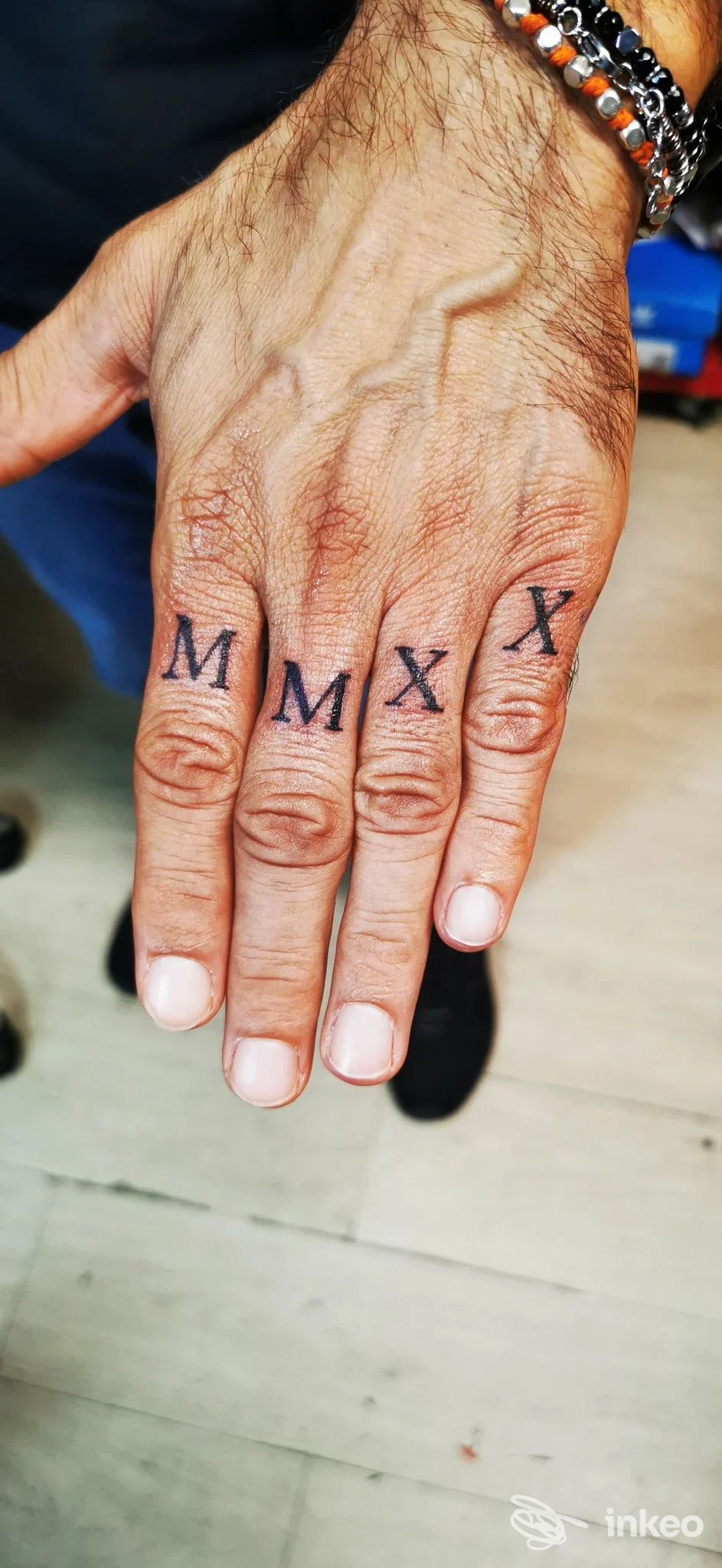 Prima inquadratura di una mano con tatuaggi sulle nocche ('MMXX'), realizzati da Ink On Show Tattoo e Piercing a Rimini.