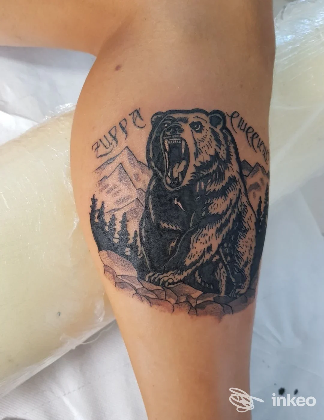 Tatuaggio di un orso ruggente con montagne e foresta sul polpaccio, realizzato da B-Max Tattoo a Casalgrande.