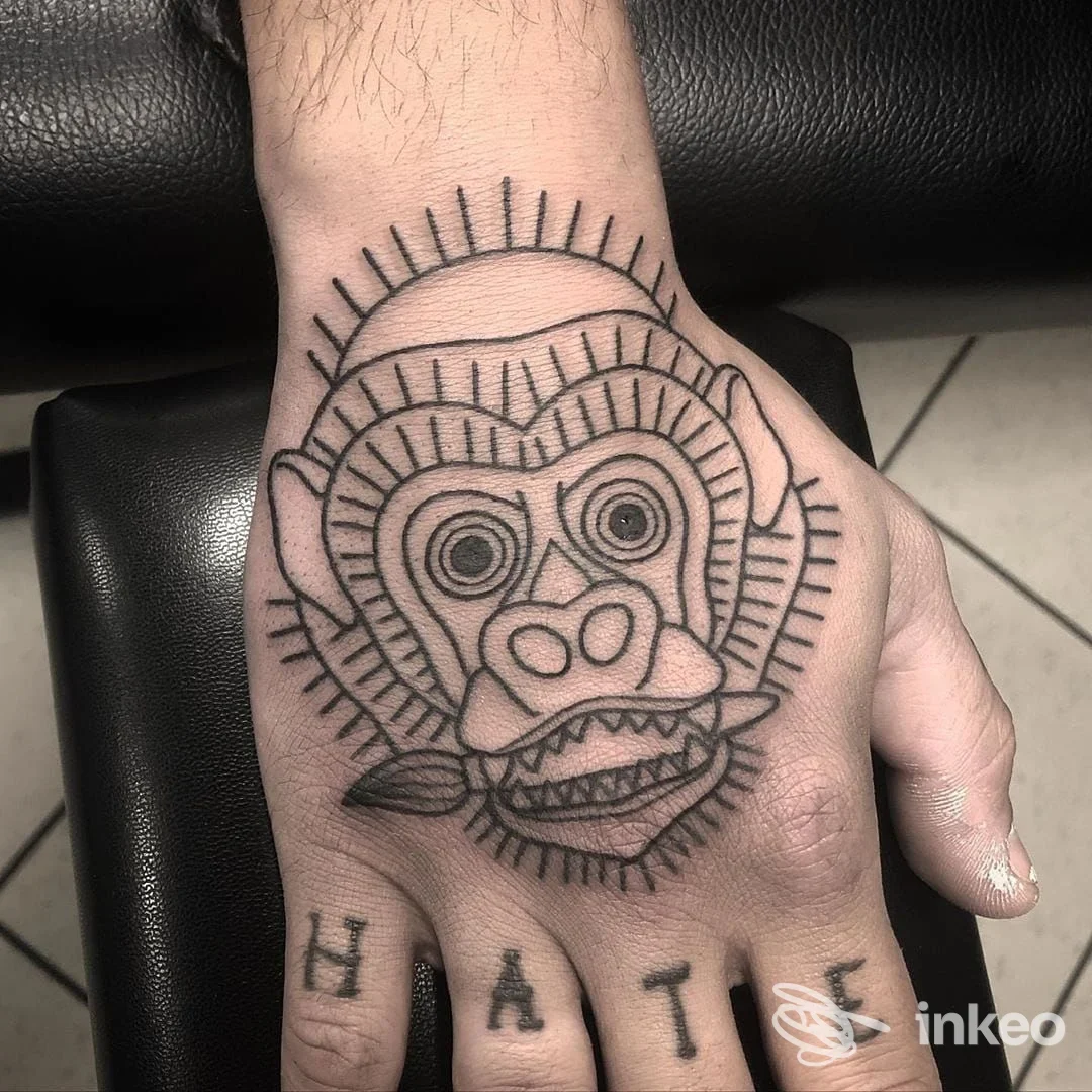 Tatuaggio a linee nere di una maschera/scimmia sul dorso della mano, foto portfolio per Tropical Tattoo, Guastalla.