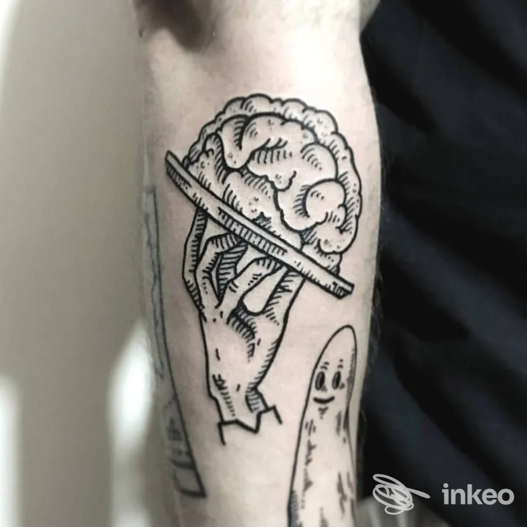 Tatuaggio su avambraccio con mano che regge un cervello e piccolo fantasma, foto fornita da Tropical Tattoo, Guastalla.