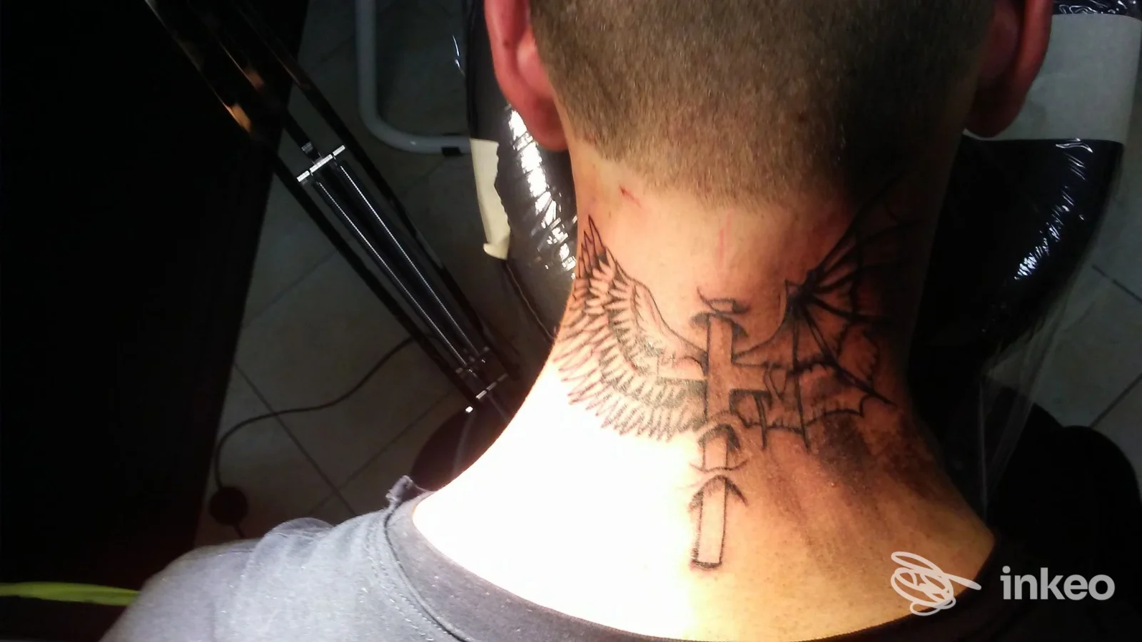 Tatuaggio nero con ali e croce/chiave sulla nuca, fotografia dal vivo dello studio Ludipea Tattoo a San Pietro in Casale.