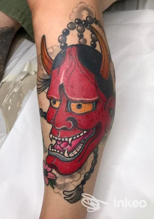 Tatuaggio su polpaccio: grande maschera demoniaca rossa con corna e perle, lavoro di The Black Hobo Society Tattoo & Piercing, Bologna.