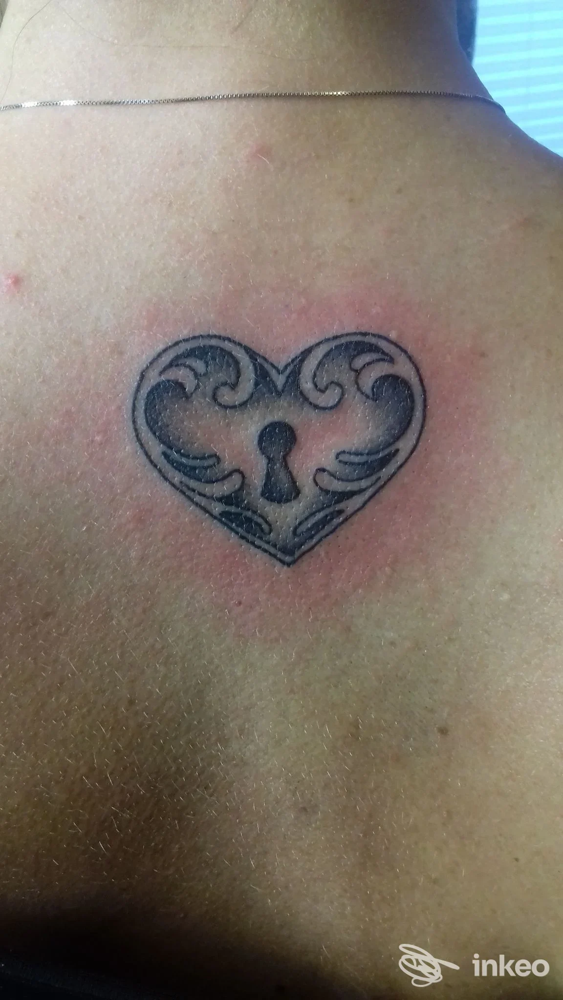 Tatuaggio a forma di cuore con serratura sulla parte alta della schiena, foto fornita da Absinthium Tattoo Studio, Spilamberto.