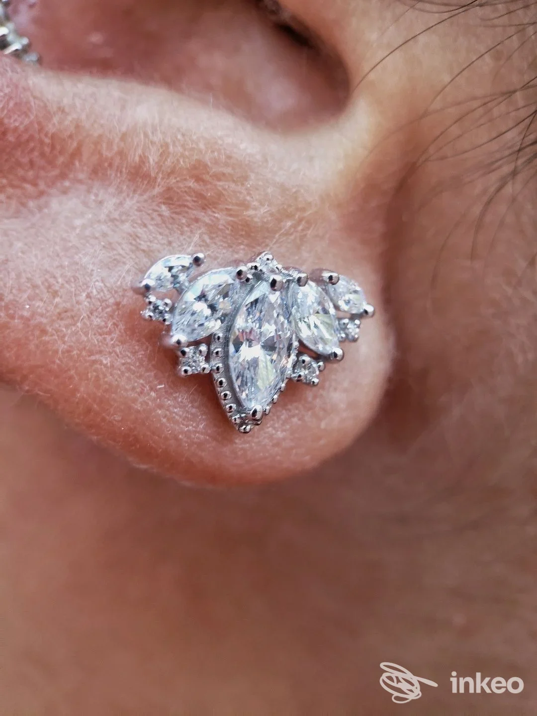 Piercing sull'orecchio con gioiello argentato luminoso, primo piano sull'orecchio sinistro.