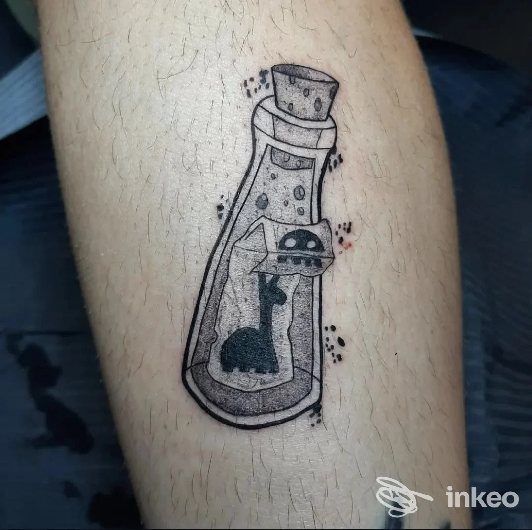 Tatuaggio su avambraccio raffigurante una bottiglia con all'interno la silhouette di un gatto e un piccolo UFO, scattato da Ivy Tattoo Studio, Gradisca d'Isonzo.