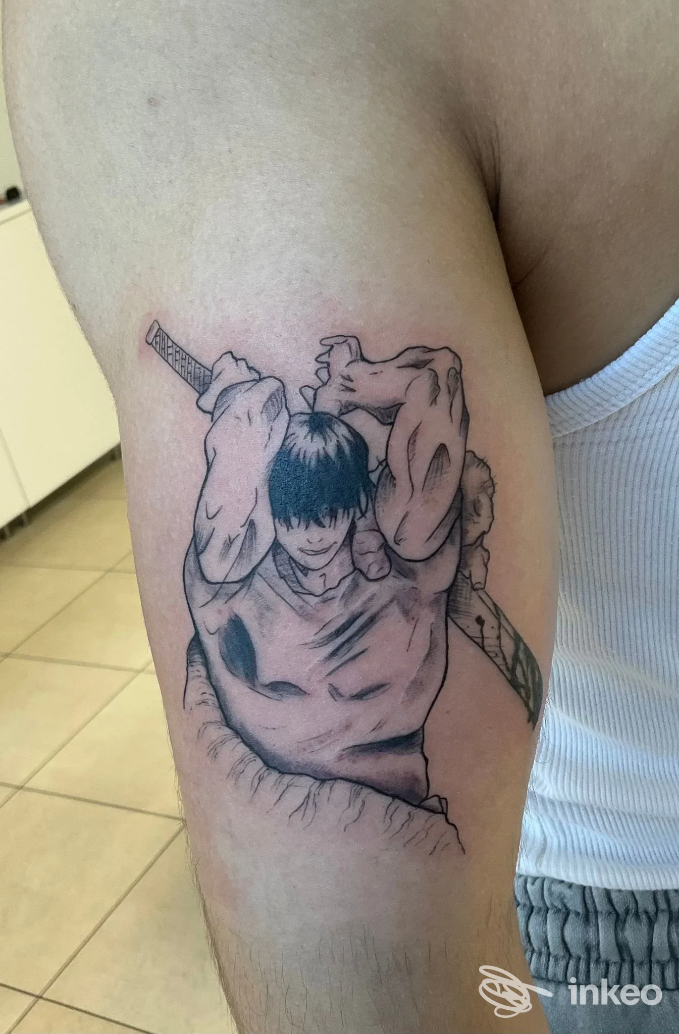 Tatuaggio in stile manga sul bicipite eseguito da WANDERLUSTATTOO, Buia: figura maschile con spada in nero e sfumature grigie.