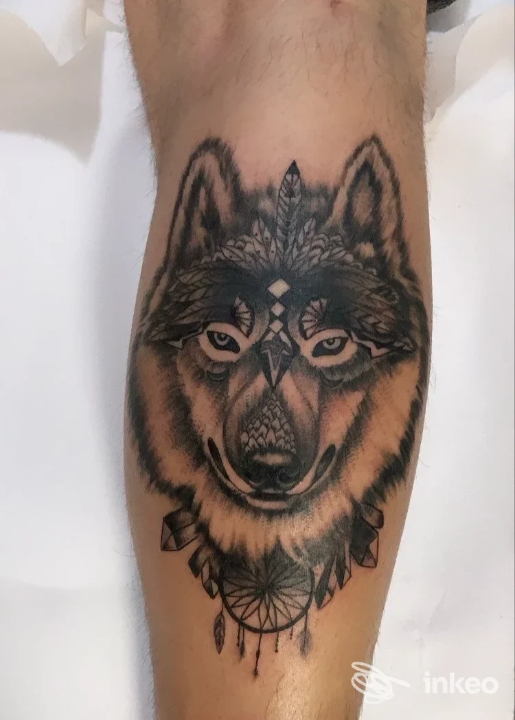 Tatuaggio di un lupo con elementi ornamentali e dreamcatcher sul polpaccio, realizzato da Custom Way Tattoo a Gorizia.