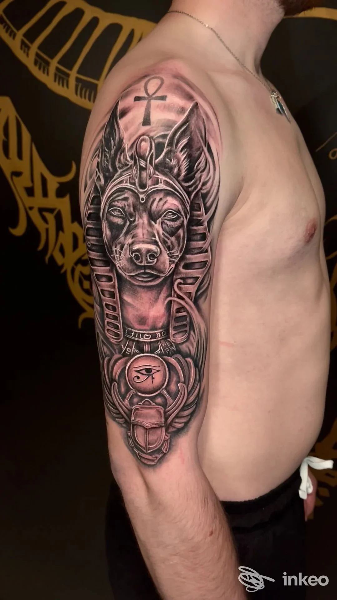 Uomo di profilo con grande tatuaggio in stile egizio sull'omero e parte superiore del braccio; foto dello studio Old Skull - Tattoo Garage, Pordenone.