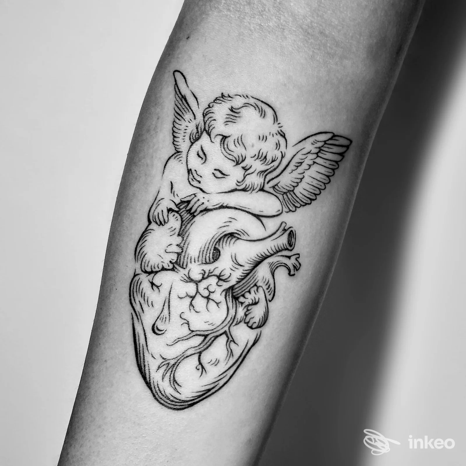 Tatuaggio in nero di un angelo che poggia su un cuore anatomico sull'avambraccio, realizzato da AufBau Tattoo a Udine.