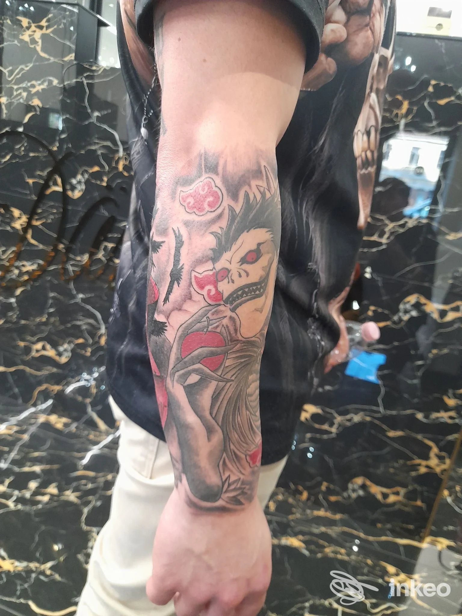 Tatuaggio sul braccio sinistro di un teschio stilizzato con particolari rossi e dettagli scuri, accompagnato da elementi decorativi.
