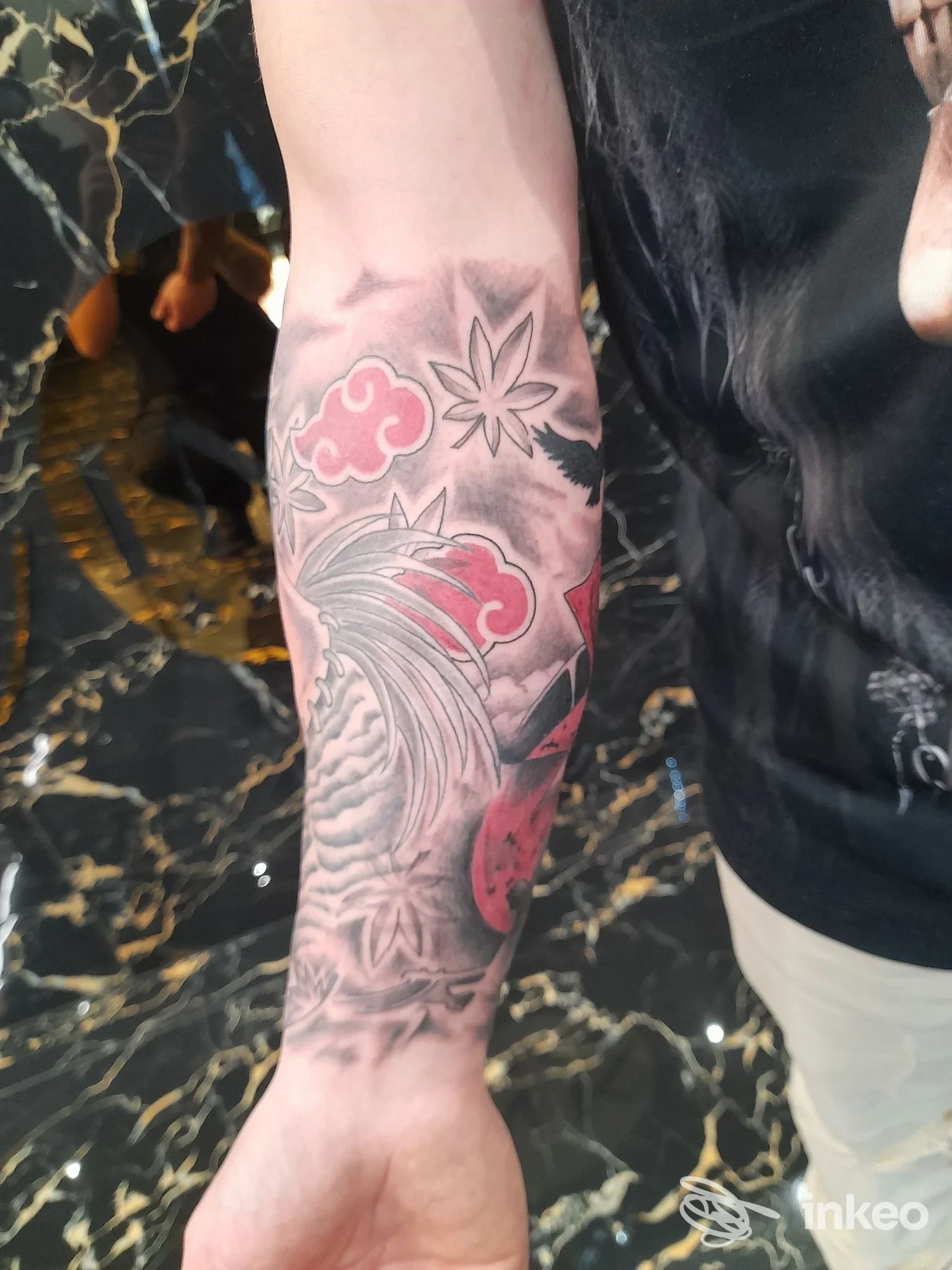 Braccio con tatuaggio visibile: motivi di nuvole rosse e onde, con una foglia d'acero, su sfondo scuro, nessun volto visibile.