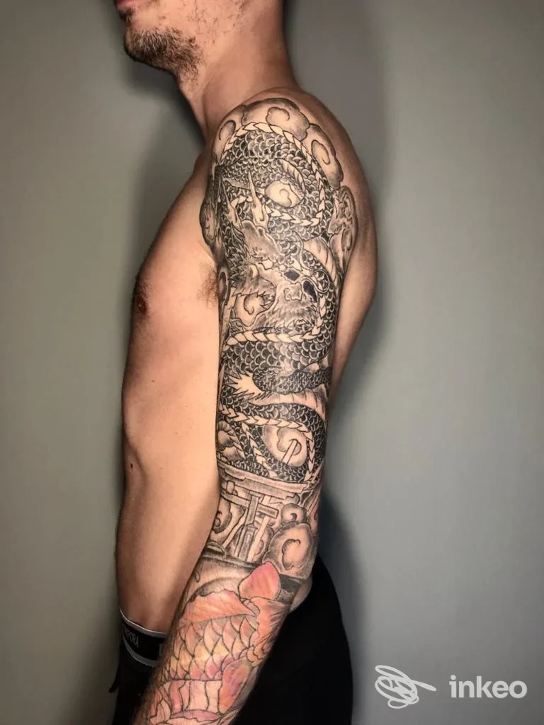 Manica tatuaggio visibile su braccio destro, fotografia di profilo che mostra dettagli neri e aree colorate; immagine fornita da Yomi Tattoo Studio, San Vito al Tagliamento.