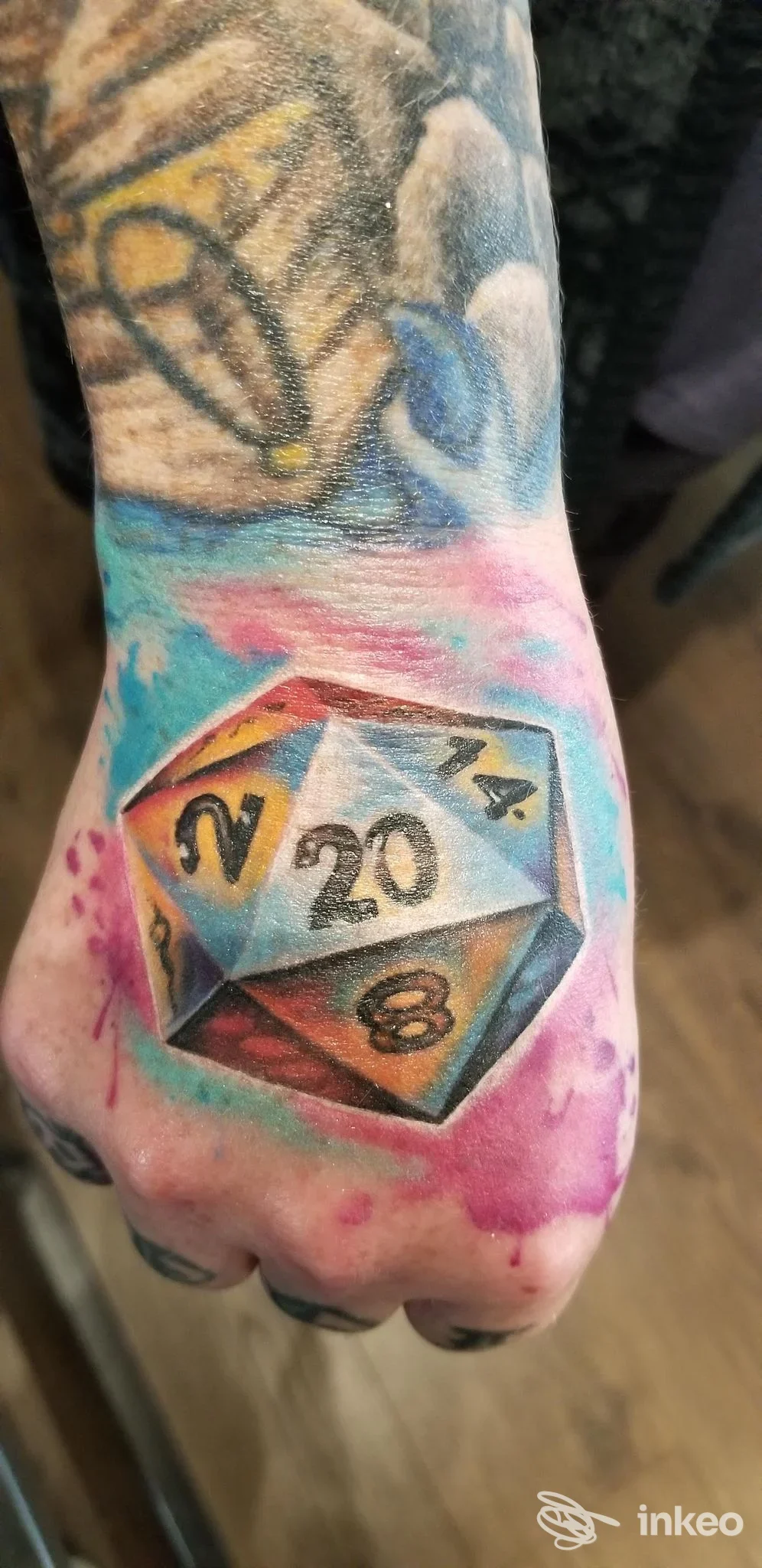 Tatuaggio colorato raffigurante un dado a 20 facce in prospettiva sul dorso della mano, fotografia singola. Upbeat Tattoo studio, Sacile.