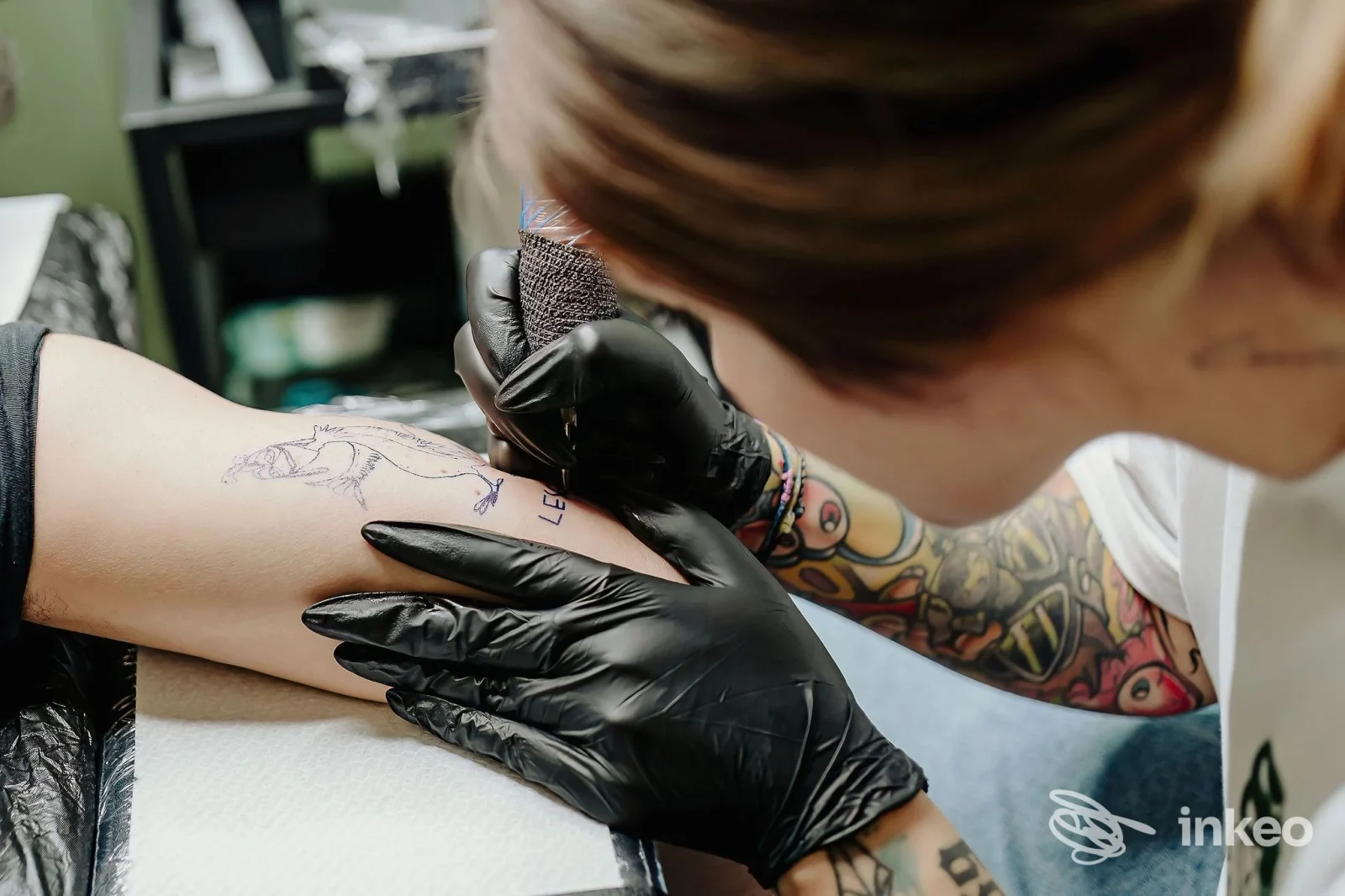 Artista che tatua l'avambraccio di un cliente nello studio Opal Tattoo & Beauty Studio a Udine, primo piano sull'atto di tatuare.