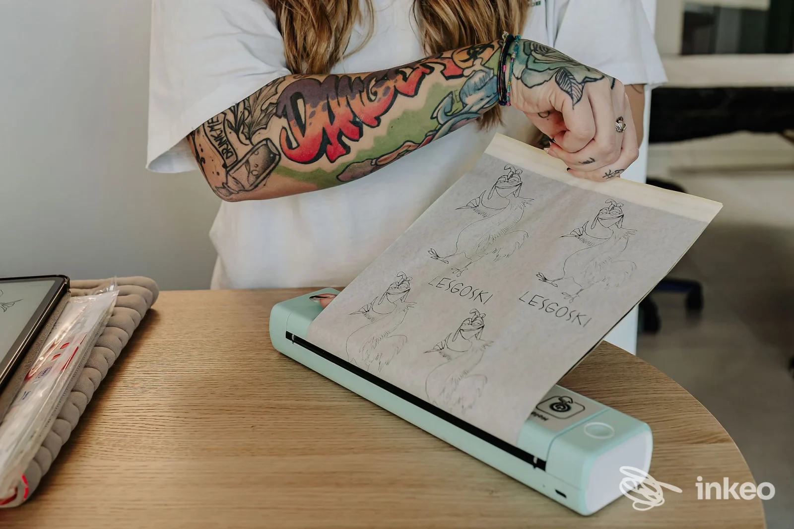Primo piano delle braccia tatuate di una persona mentre tiene fogli con disegni nello studio Opal Tattoo & Beauty Studio, Udine.