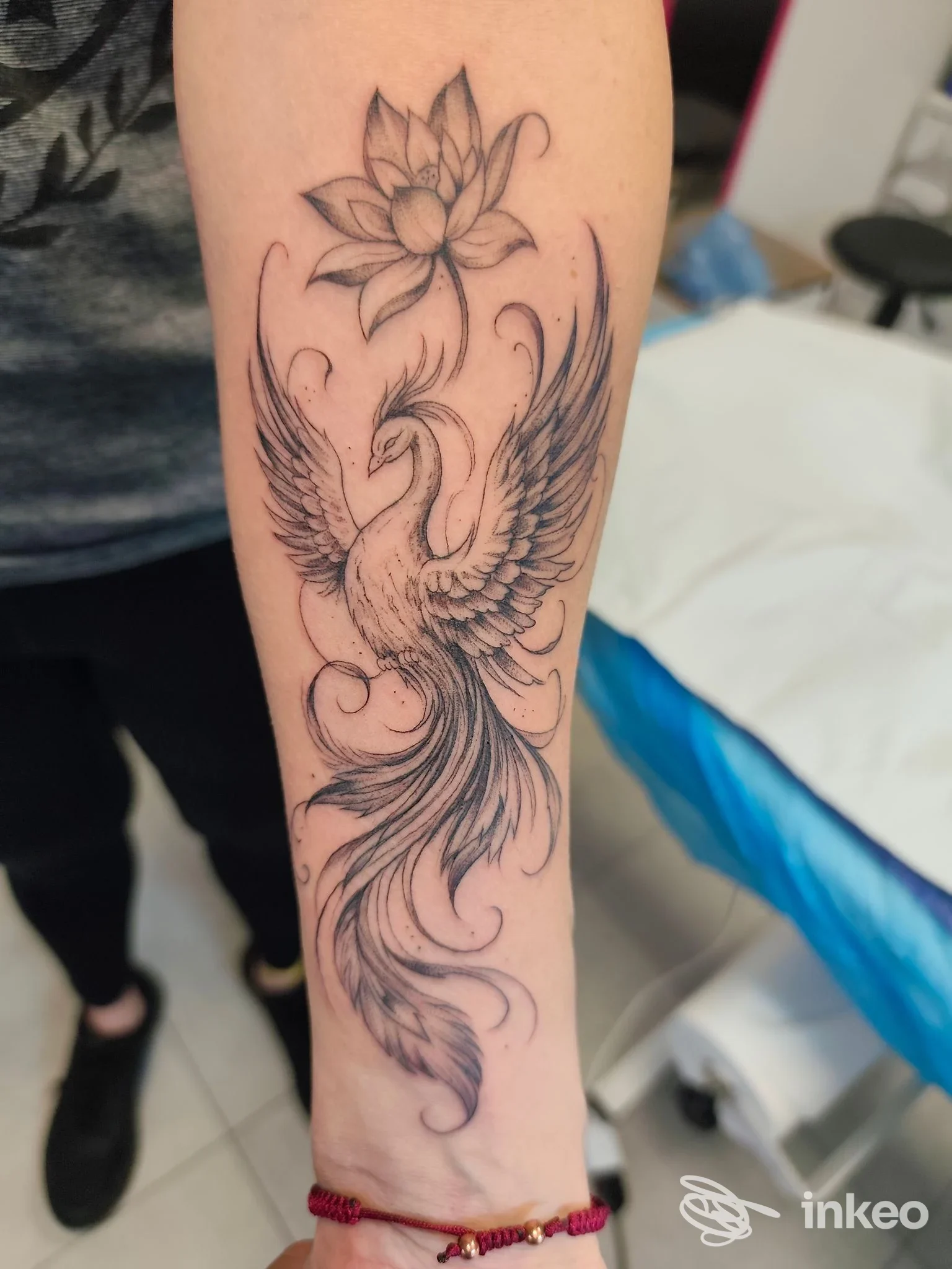 Avambraccio con tatuaggio di fenice stilizzata e fiore di loto, lavoro di Pinkpanther Tattoo a Castello d'Aviano.