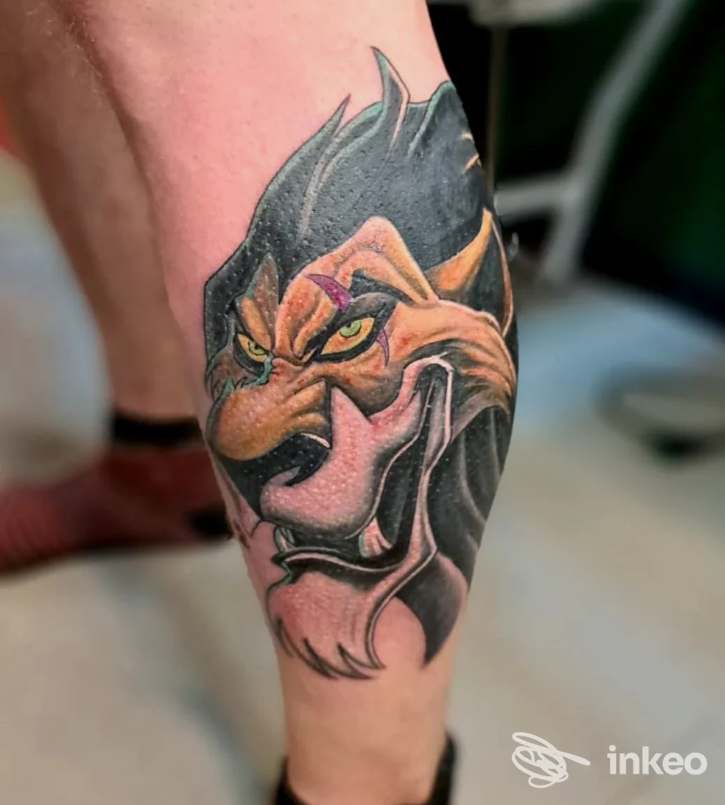 Tatuaggio a colori raffigurante il volto stilizzato di un leone sul polpaccio, lavoro di Second Skin, Trieste.