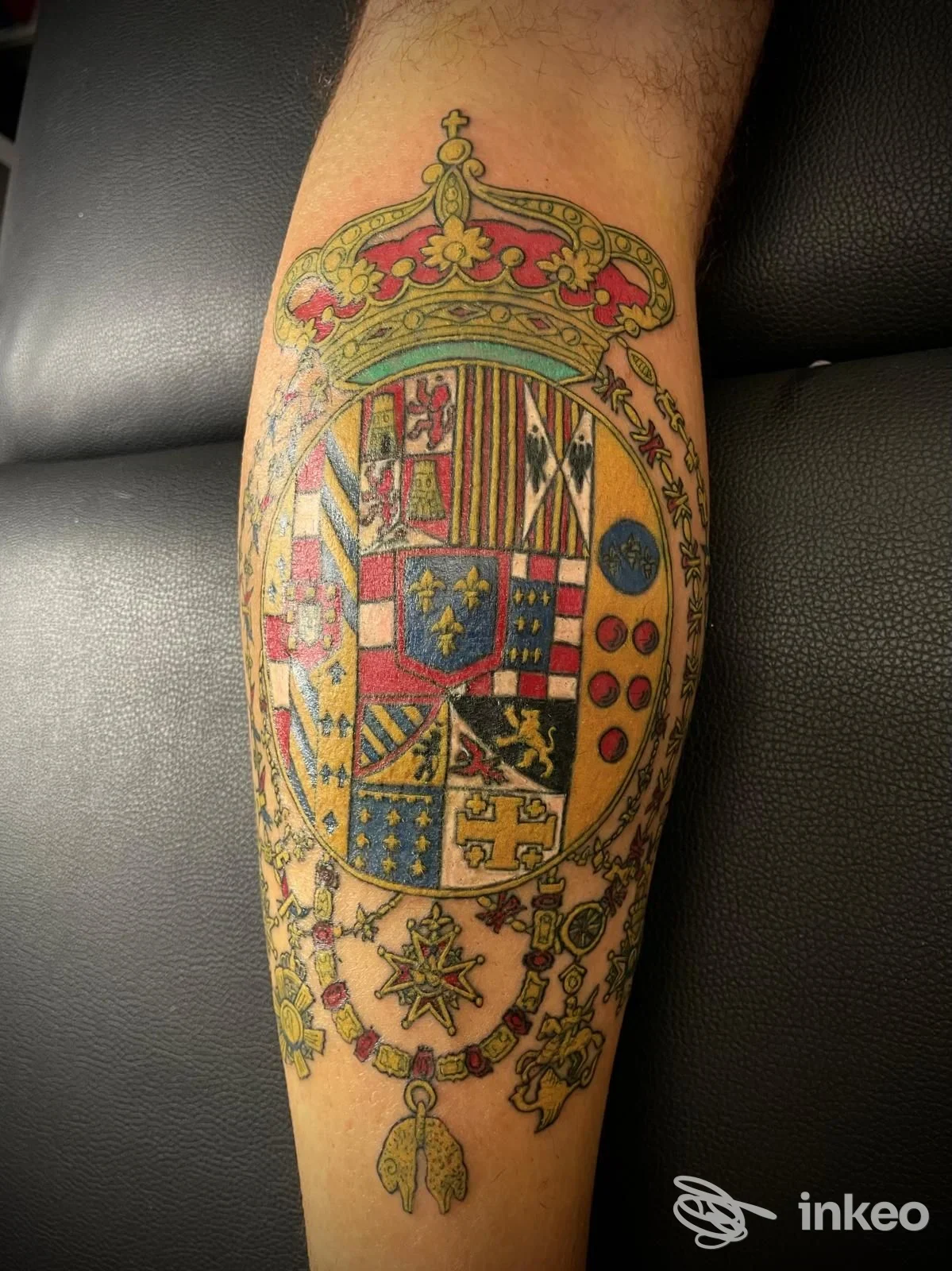 Tatuaggio araldico coronato sul polpaccio, foto fornita da Pitt Tattoo Studio, Udine; stemma colorato con dettagli ornamentali.