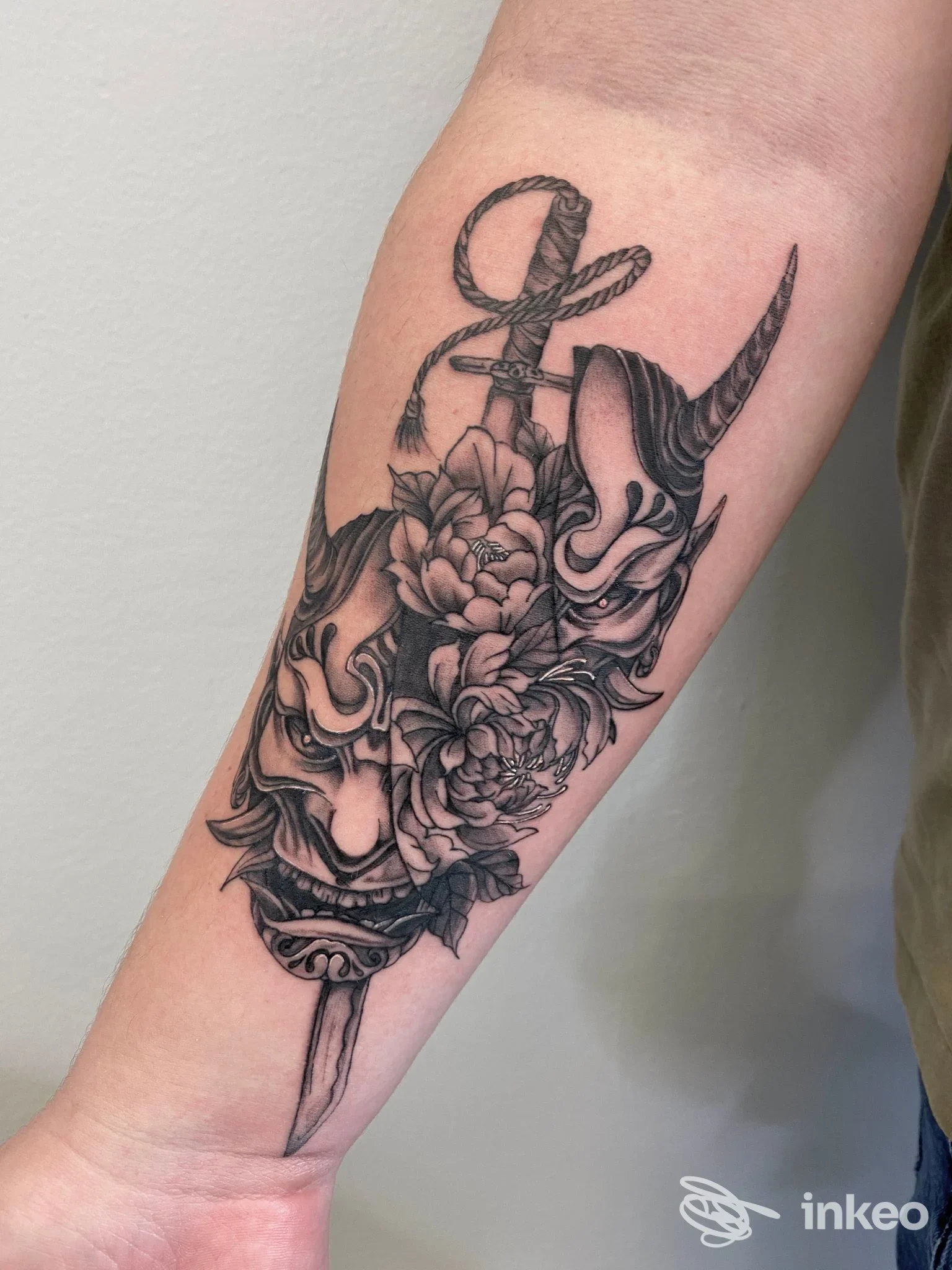 Tatuaggio in bianco e nero con maschere, fiori e pugnale sull'avambraccio, Tattoo Crew Aviano, Aviano.