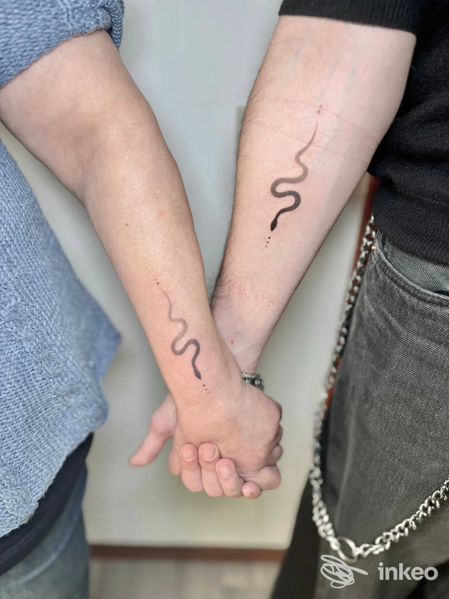 Due avambracci che si tengono per mano con piccoli tatuaggi a serpente in nero, immagine fornita da TATTY.INK tattoo studio, Manzano.