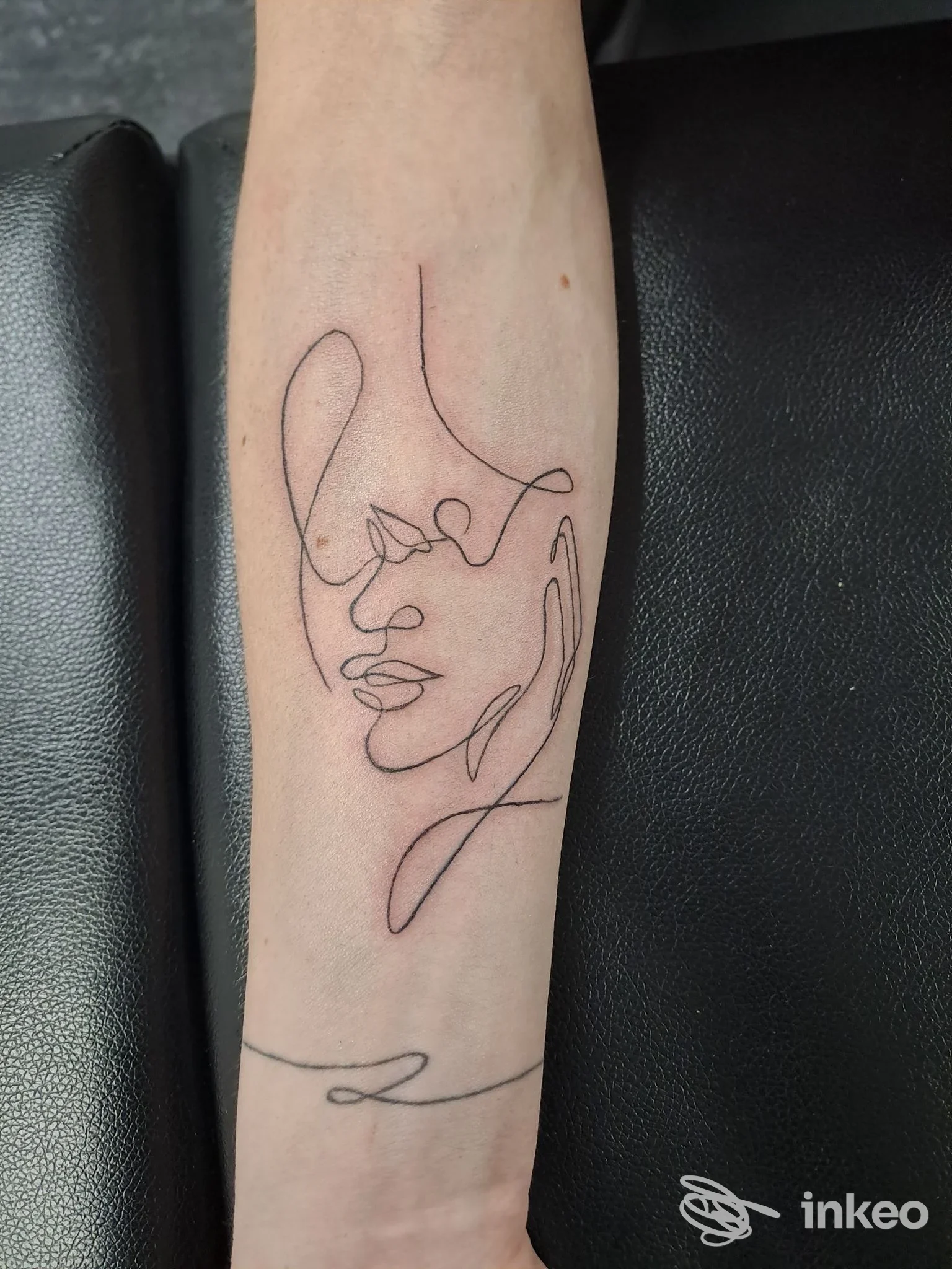 Fotografia di un avambraccio con un tatuaggio a linea continua che raffigura un volto stilizzato, senza elementi promozionali o overlay social.
