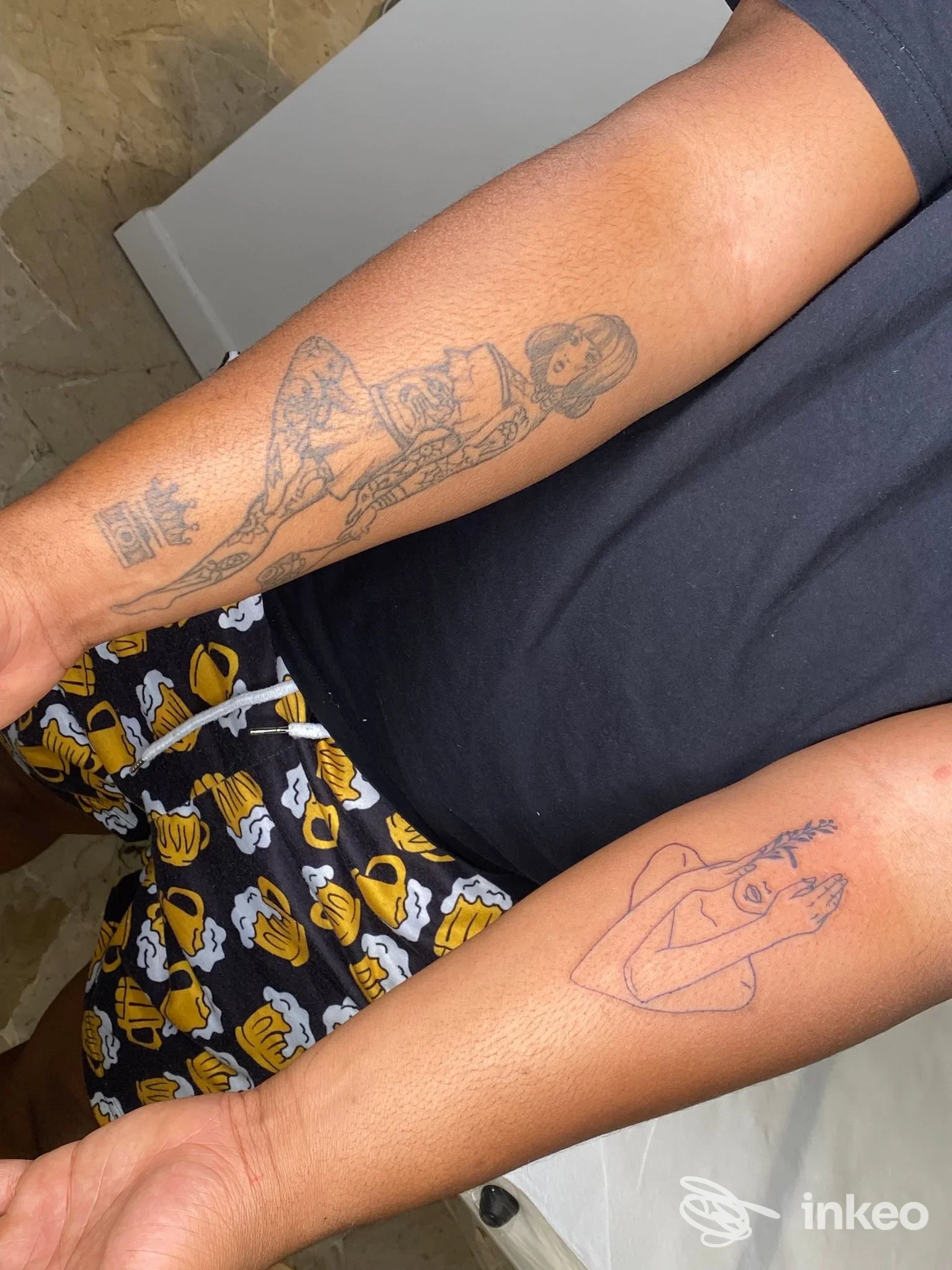 Due avambracci fotografati con tatuaggi: uno con figura femminile dettagliata e uno con bozzetto stilizzato; immagine fornita da Nero Argento a Different Shop, Cordenons.