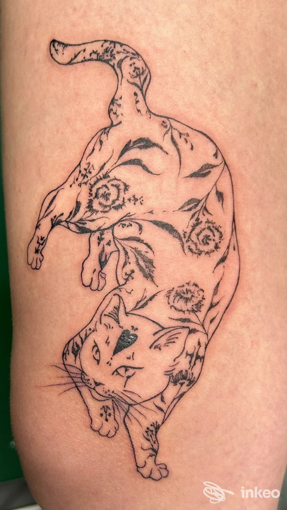 Tatuaggio a linee nere di un gatto con motivi floreali sull'avambraccio, scatto di Needless Tattoo Studio, Udine.