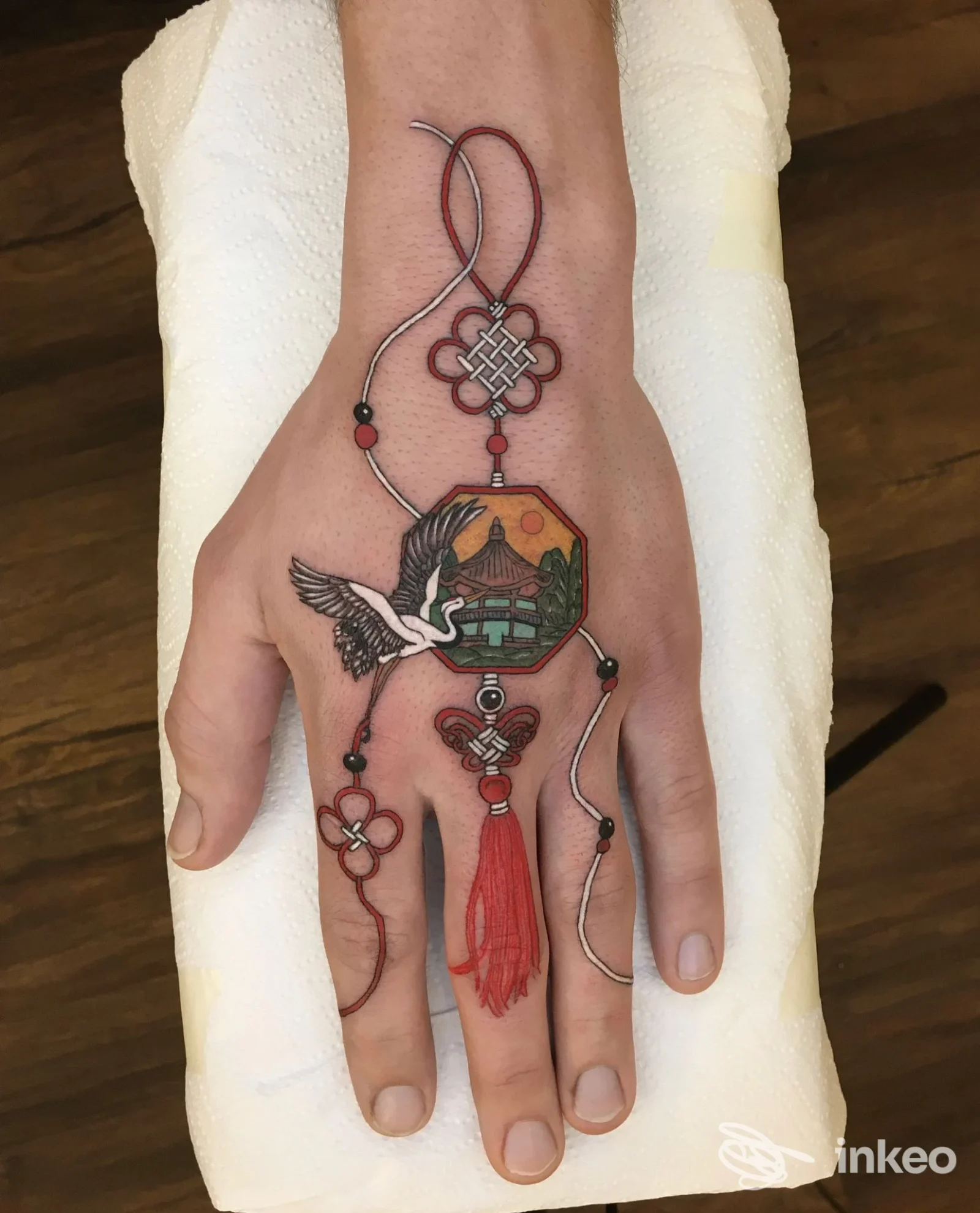 Tatuaggio colorato sul dorso della mano con ciondolo e nappina realizzato da Eremo Studio a Pordenone.